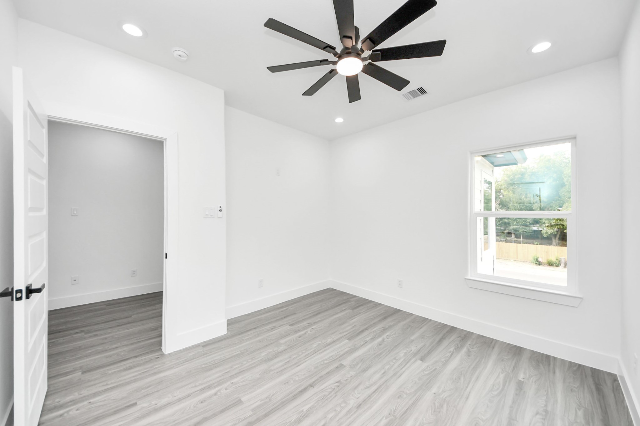 Bright and airy room featuring sleek hardwood floors, a modern ceiling fan, and ample natural light from a large window.