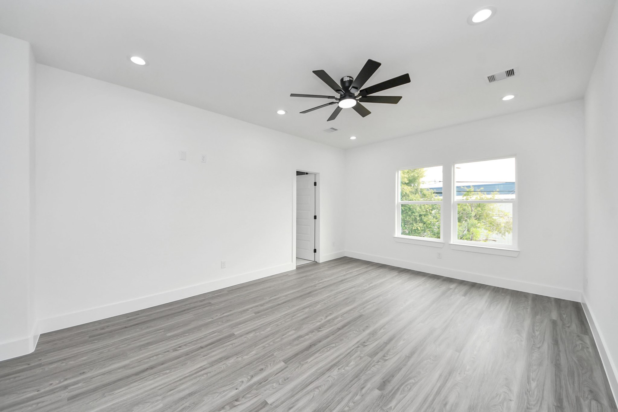 Spacious, bright room with modern wood flooring, recessed lighting, and a sleek ceiling fan, offering ample natural light through large windows.