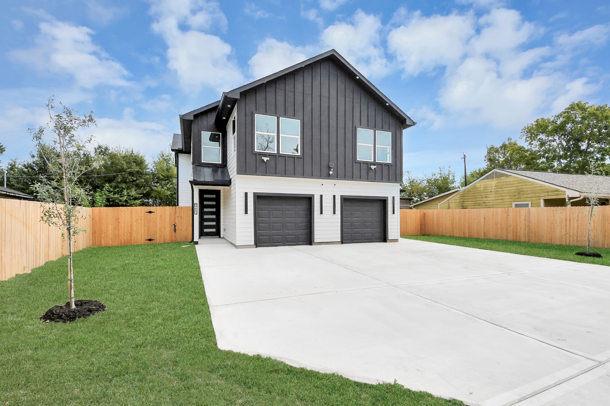 Modern two-story home with sleek dark siding, dual garage doors, and a spacious driveway, set within a neatly fenced yard.