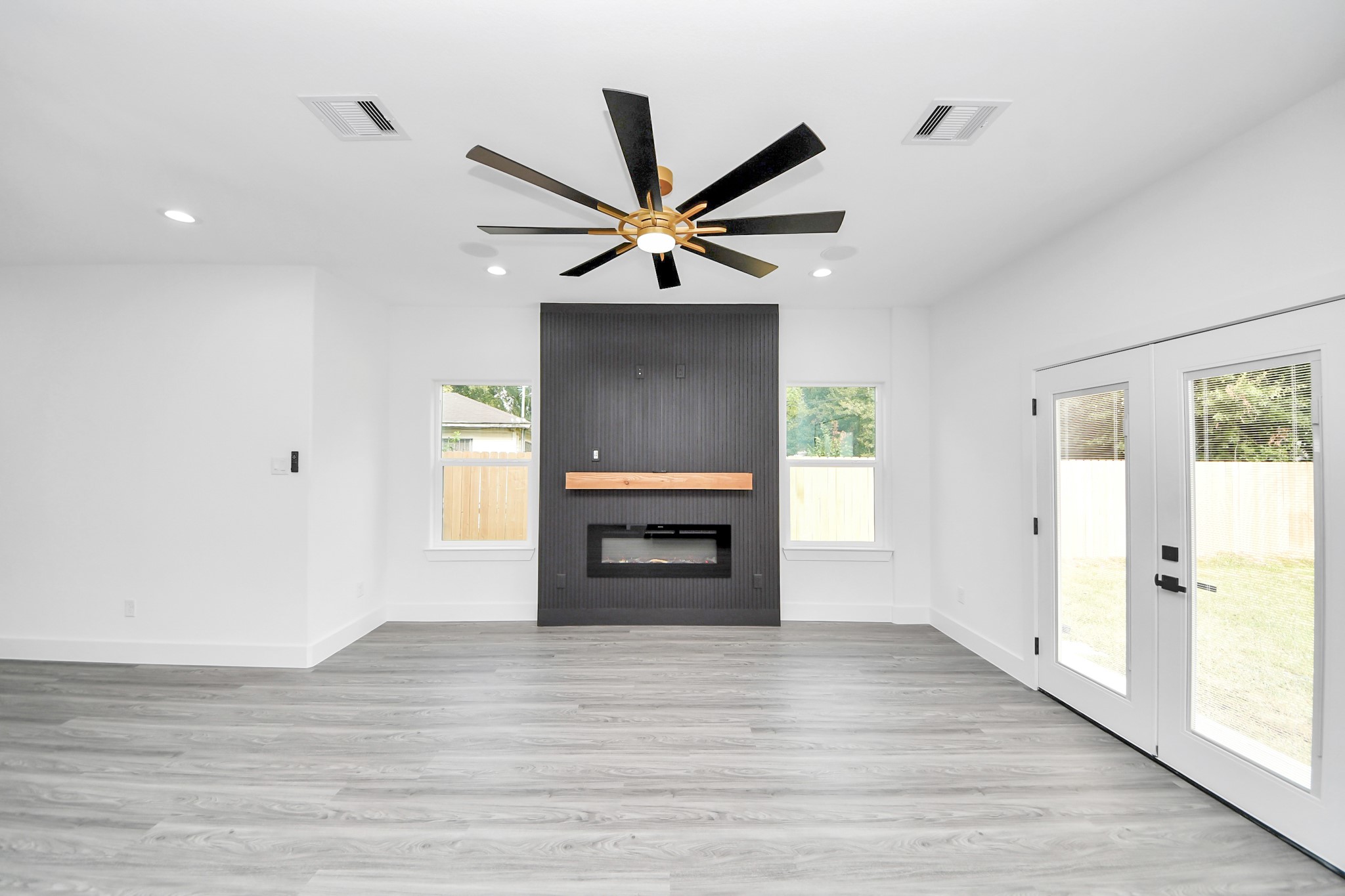Bright and modern living room featuring sleek wood flooring, a striking black accent wall with a contemporary fireplace, and elegant French doors opening to the backyard.