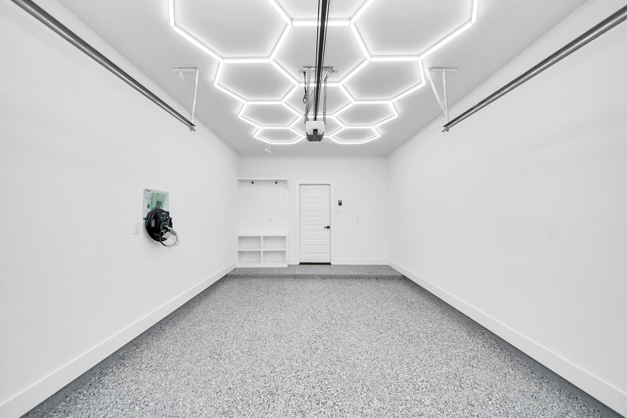 A sleek, modern garage featuring hexagonal LED lighting, pristine white walls, and an epoxy-coated floor, offering both style and functionality.