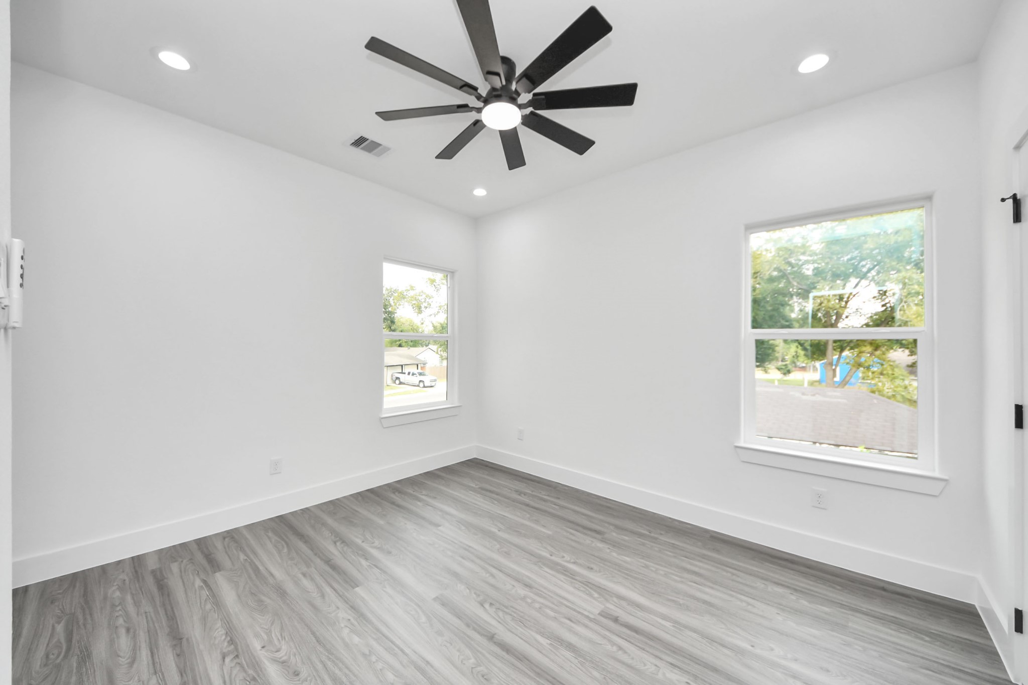 Bright and airy room featuring sleek gray flooring, modern recessed lighting, and a stylish ceiling fan, highlighted by ample natural light from two large windows.