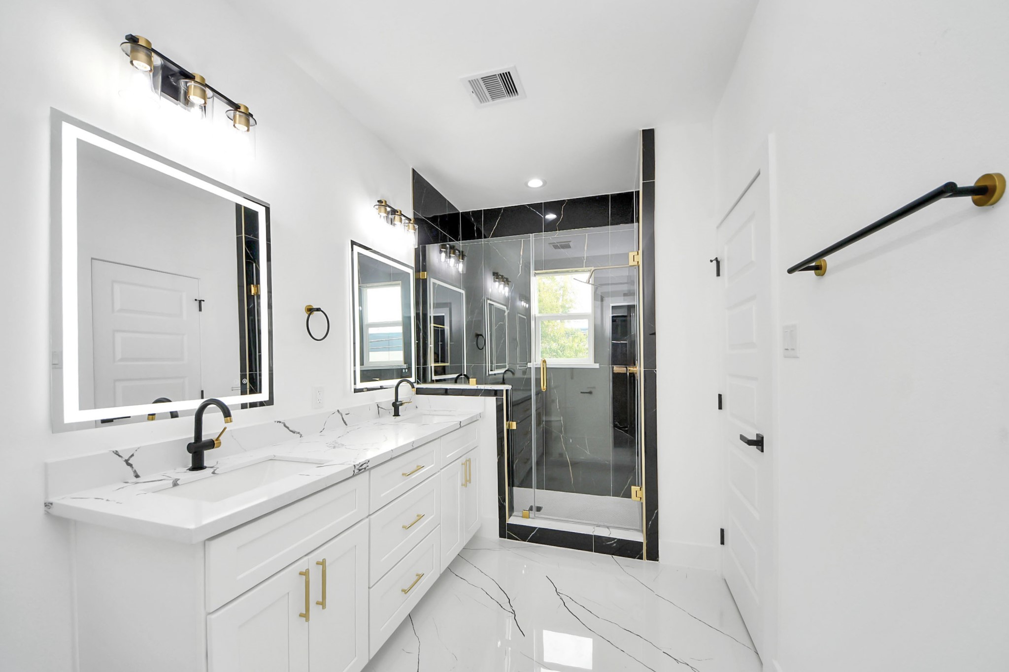 Elegant bathroom featuring a double vanity with sleek black fixtures, luxurious marble countertops, and a spacious glass-enclosed shower with gold accents.