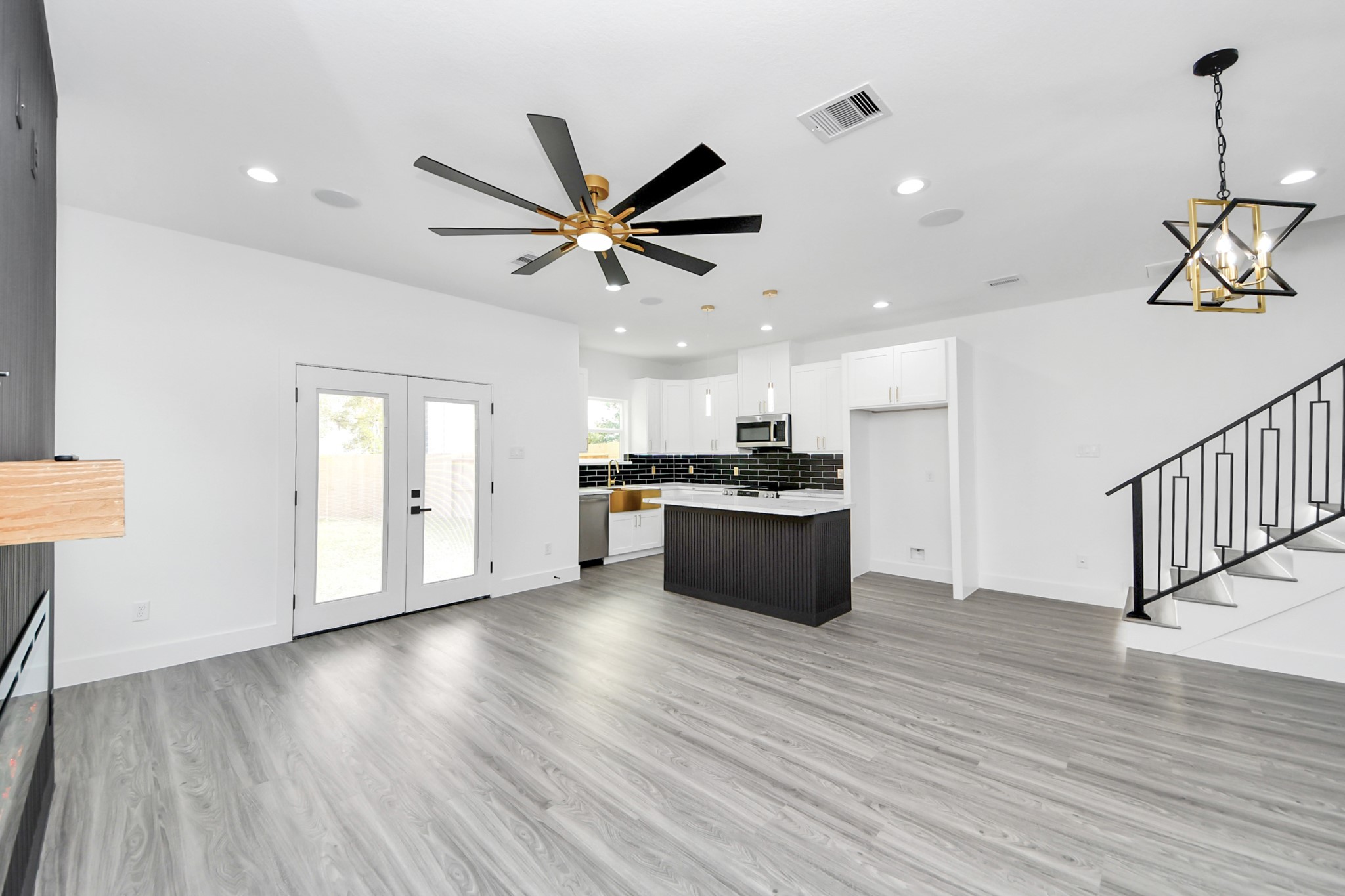 Spacious open-concept living area featuring sleek flooring, a modern kitchen with black subway tile backsplash, and stylish lighting fixtures, complemented by French doors leading to the backyard.