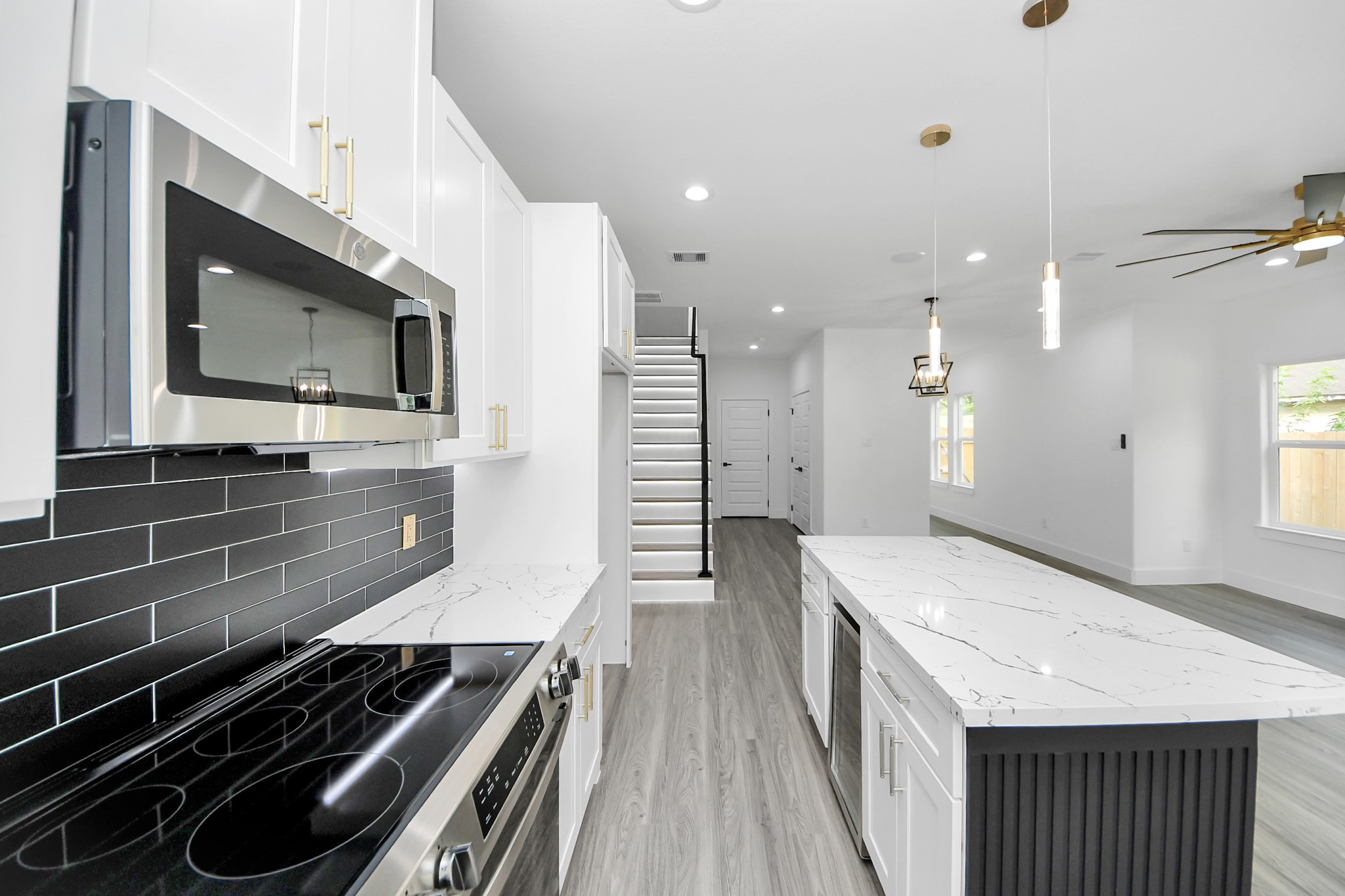 Sleek modern kitchen with a stylish black subway tile backsplash, stainless steel appliances, and a spacious marble island. Open-concept layout with elegant lighting and a contemporary staircase.