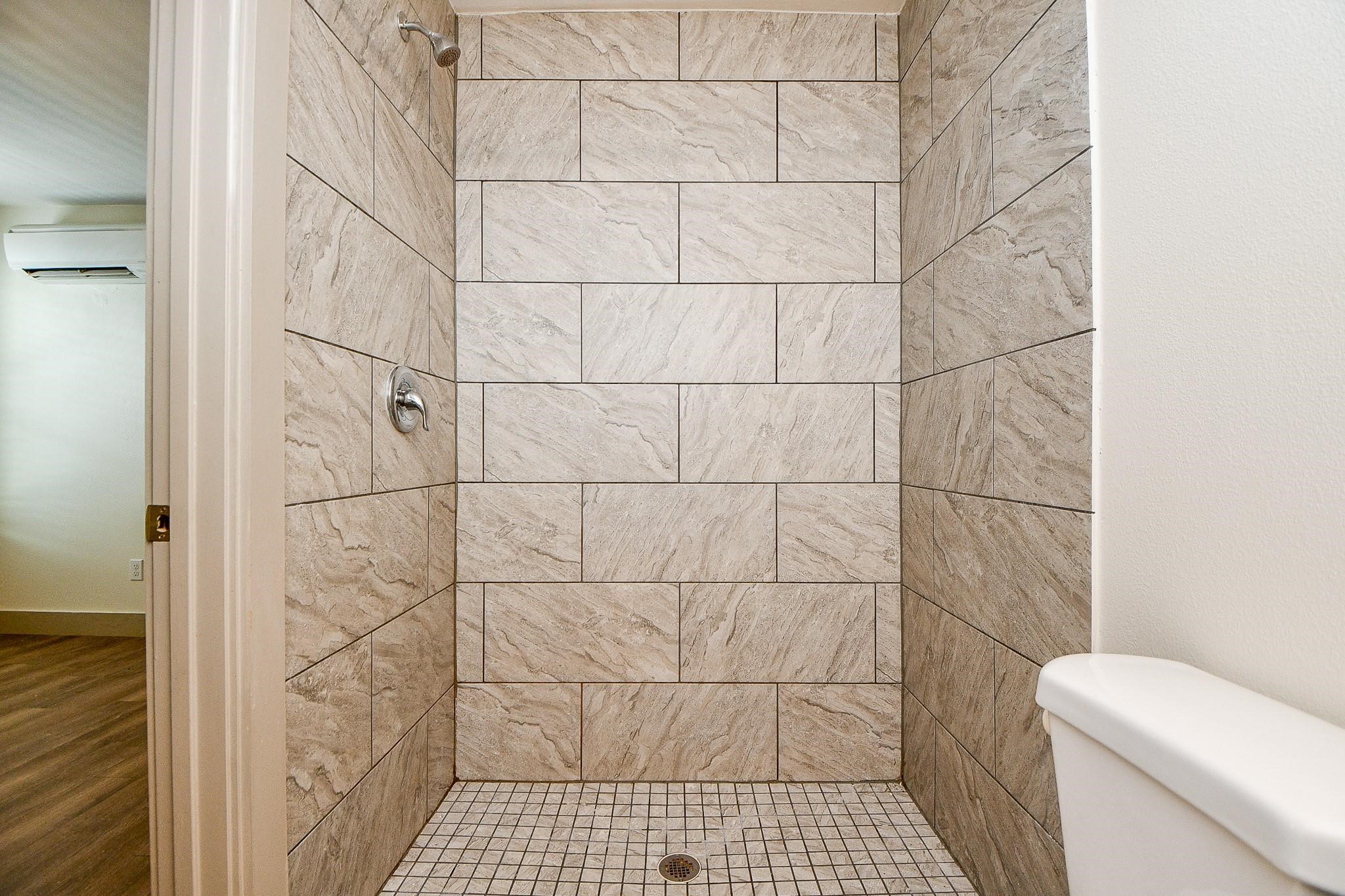 Stylish shower boasting beige tile walls and intricate small tile flooring, paired with a sleek tub for a refined look.