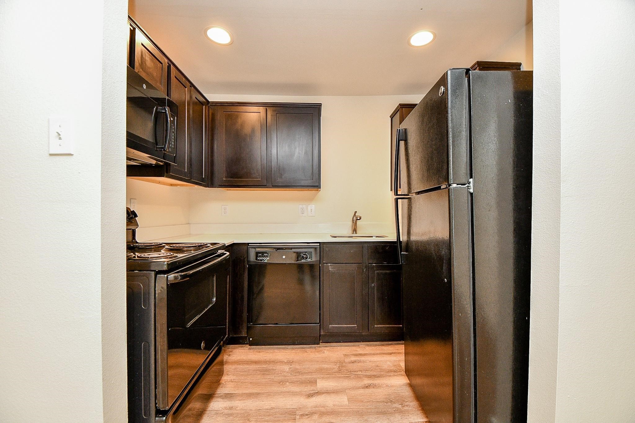 Compact, modern kitchen with dark cabinets, black appliances, and recessed lighting.