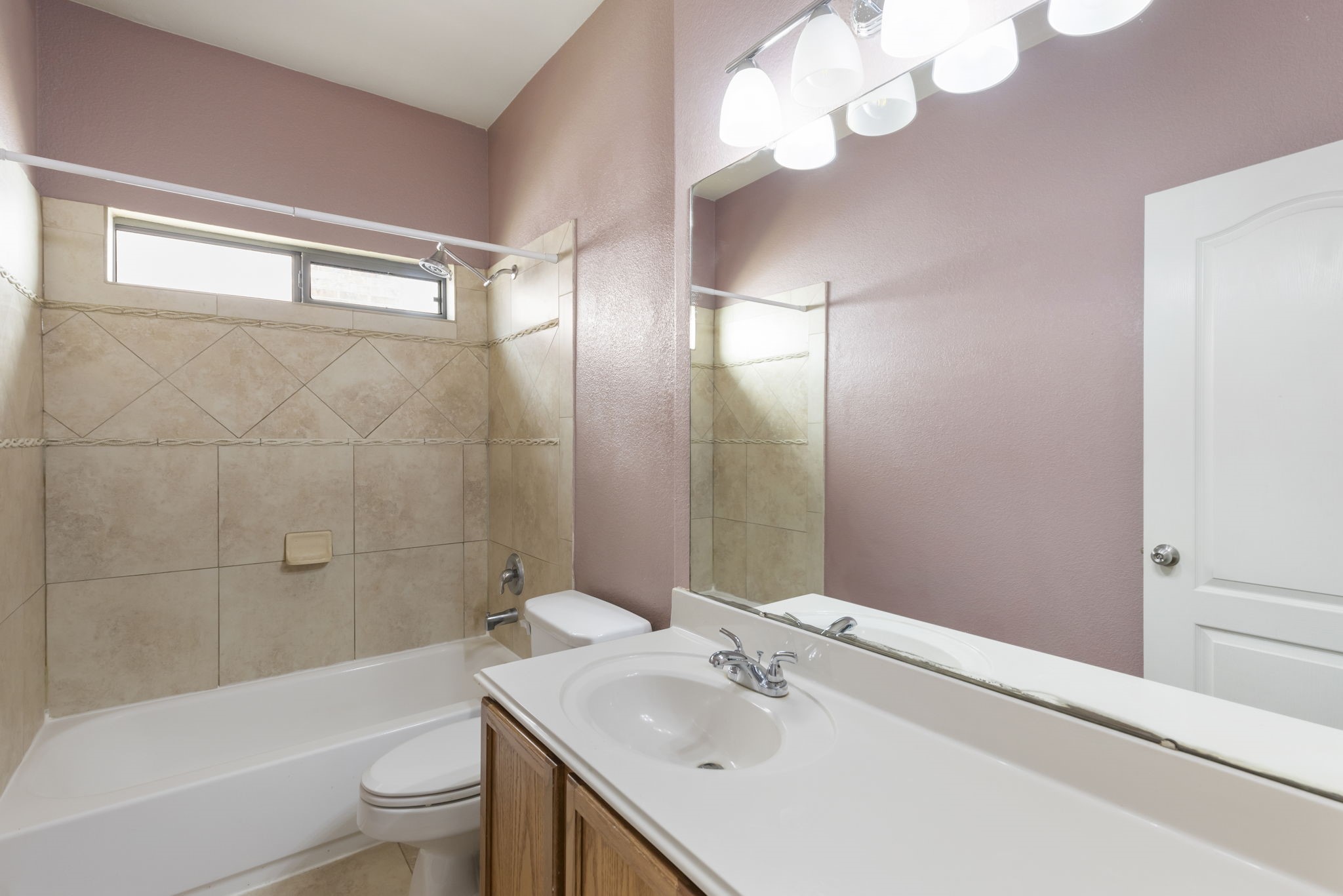 Charming bathroom with a soothing color palette, featuring a tiled shower-tub combo, large mirror, and modern lighting for a bright and inviting space.