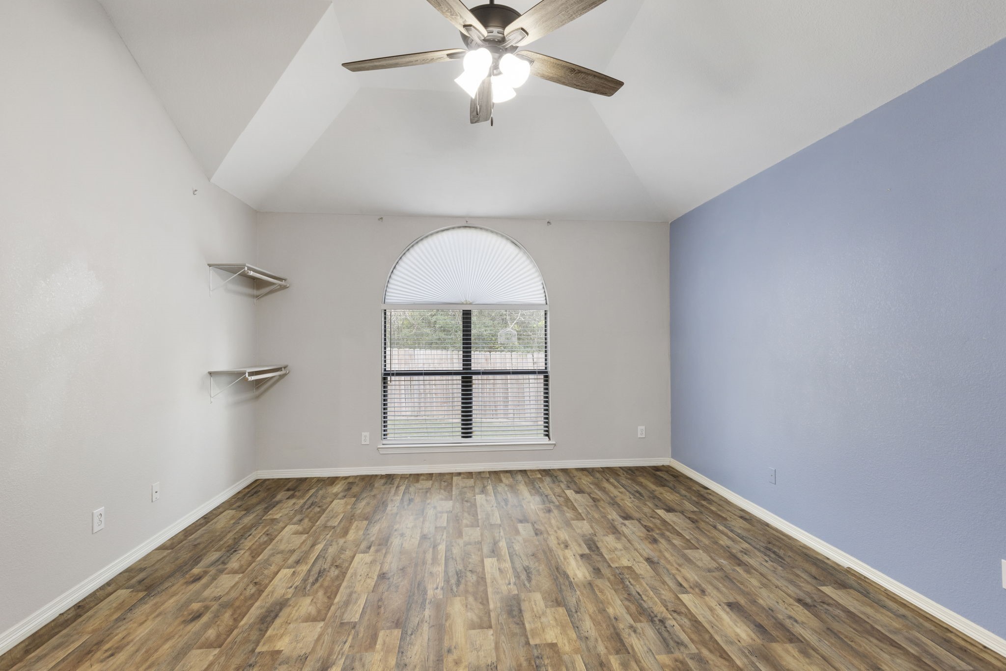 Experience serene comfort in this primary bedroom, featuring vaulted ceilings, elegant laminateflooring, and a large arched window that bathes the space in natural light.