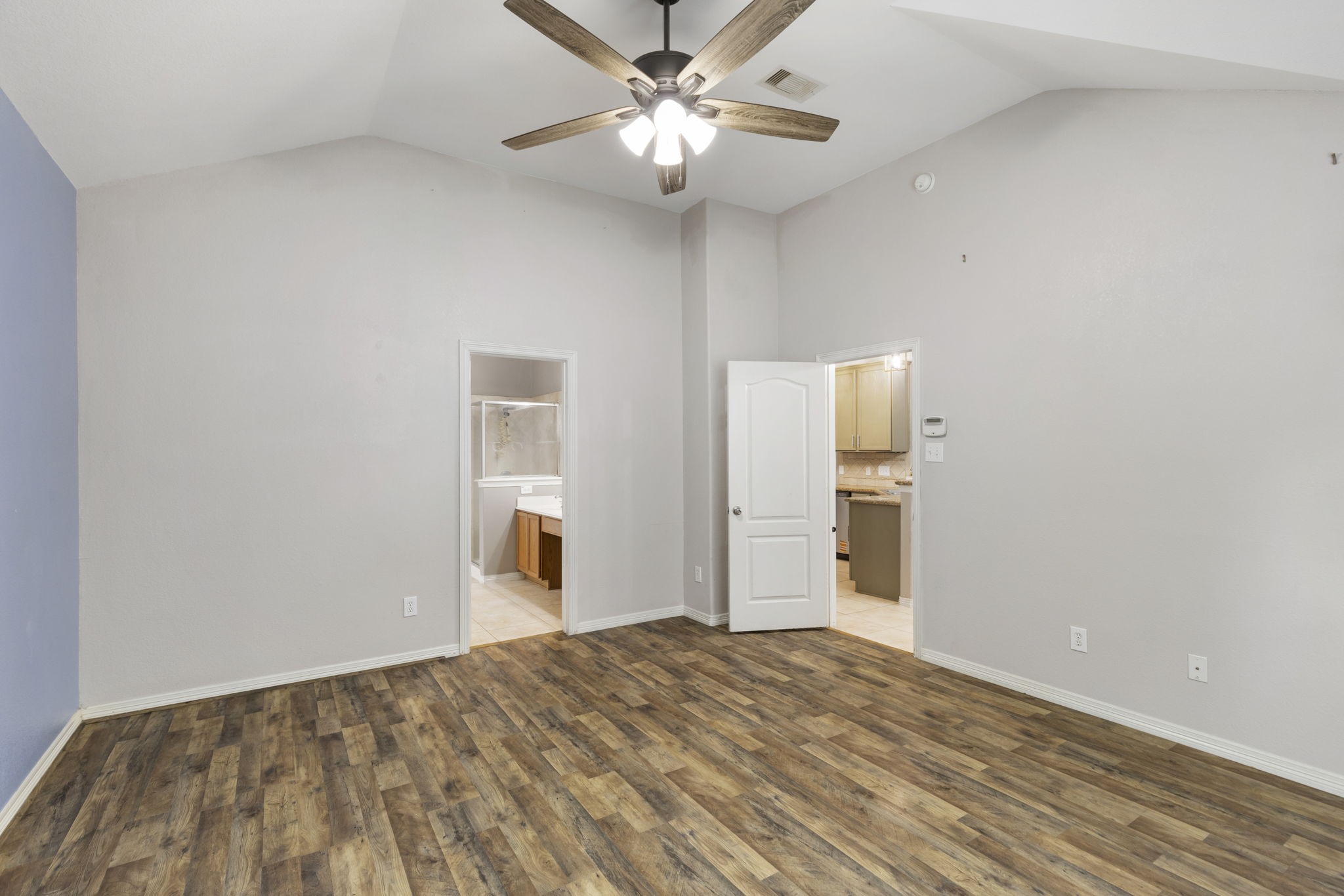 Expansive primary bedroom featuring elegant laminateflooring, vaulted ceilings with a stylish fan, and direct access to a luxurious en-suite bathroom, creating a serene and sophisticated retreat.