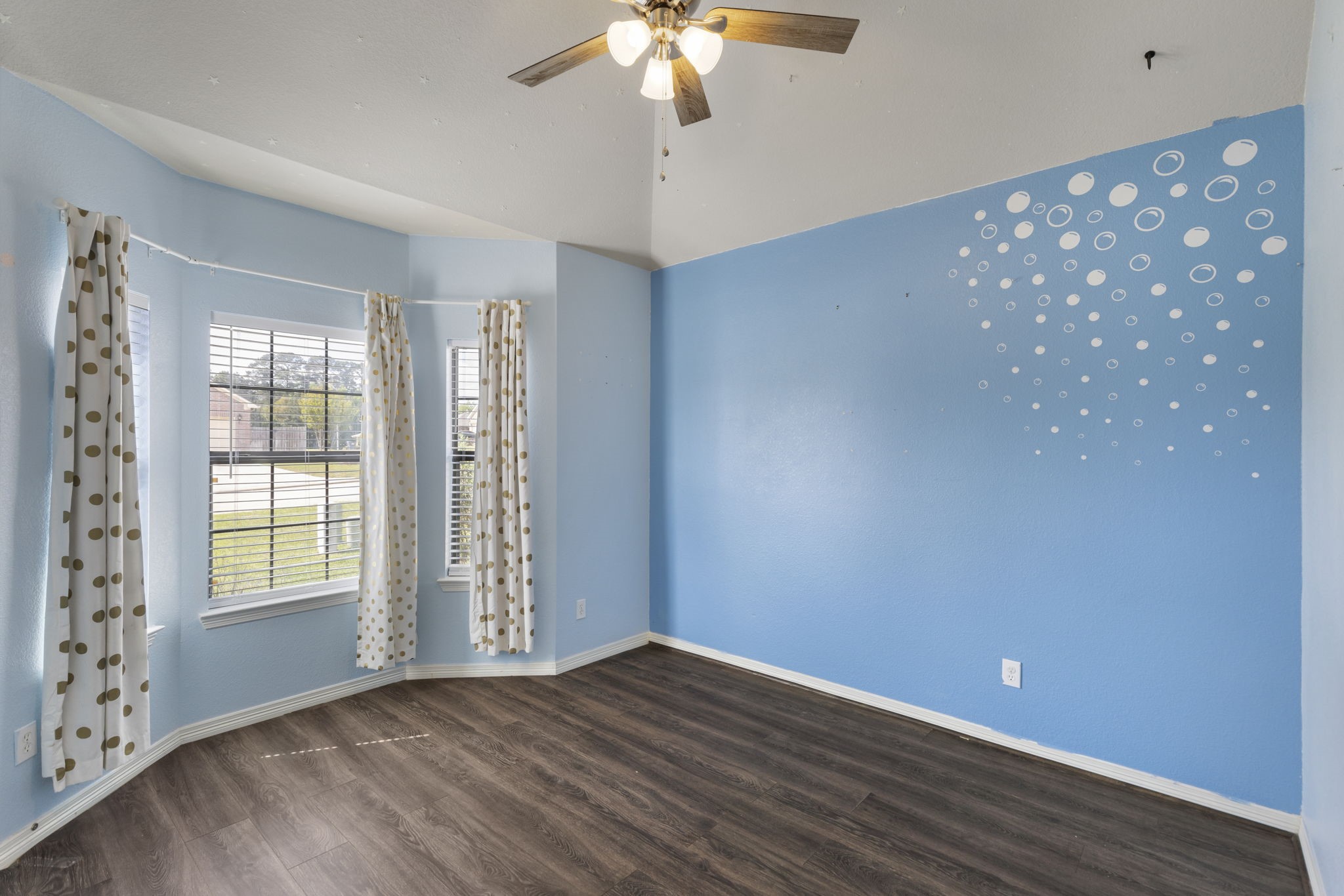 Bright and inviting room with large bay windows, charming polka dot curtains, and a whimsical bubble accent wall.