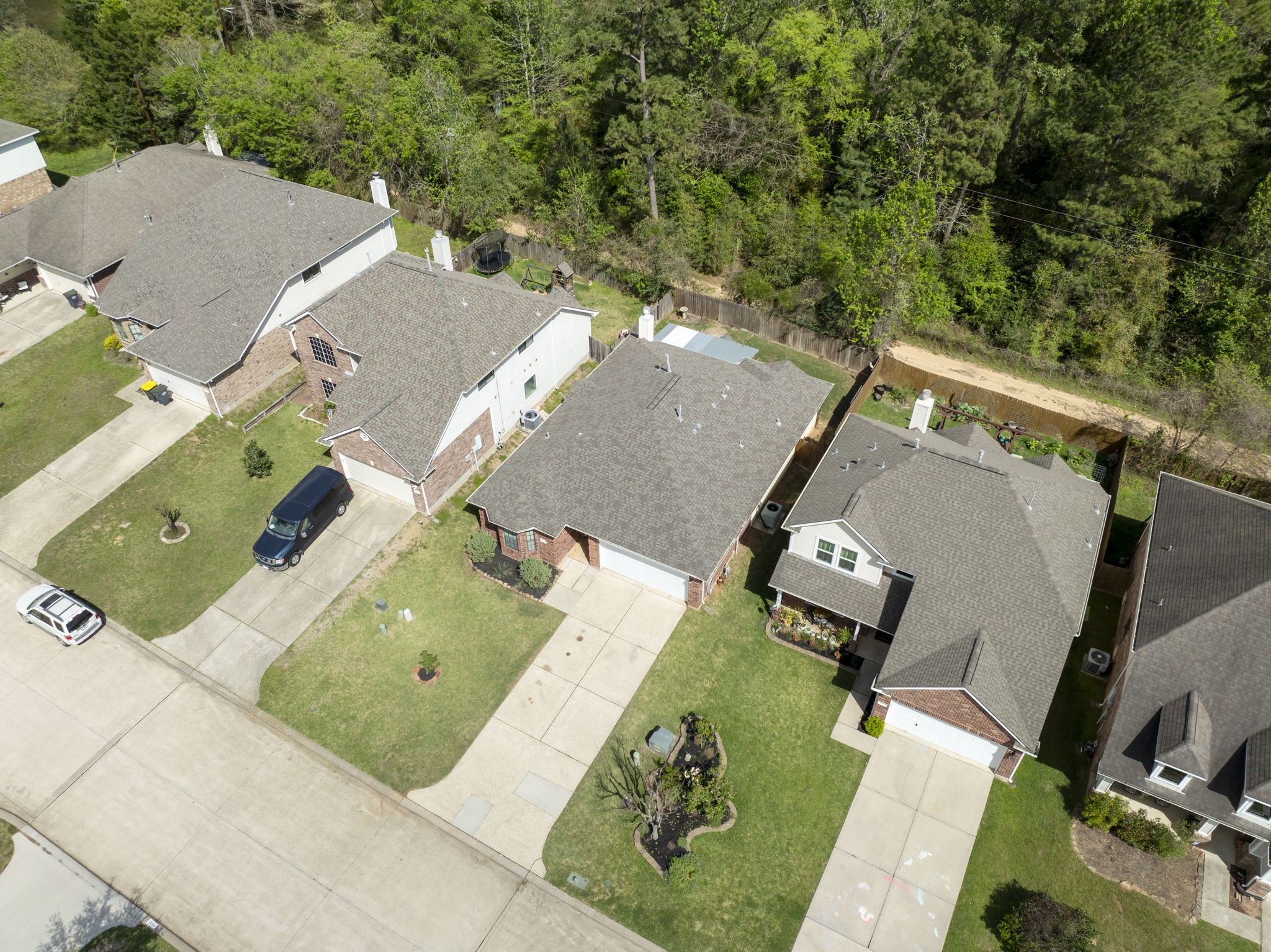 Charming suburban homes with spacious driveways and well-maintained lawns, nestled alongside a serene wooded area for added privacy and natural beauty.