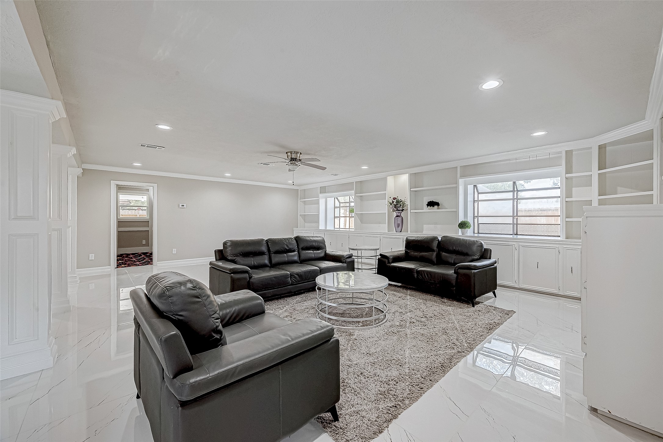 The living area includes a comfortable black leather sofa set, a central coffee table, and a ceiling fan.