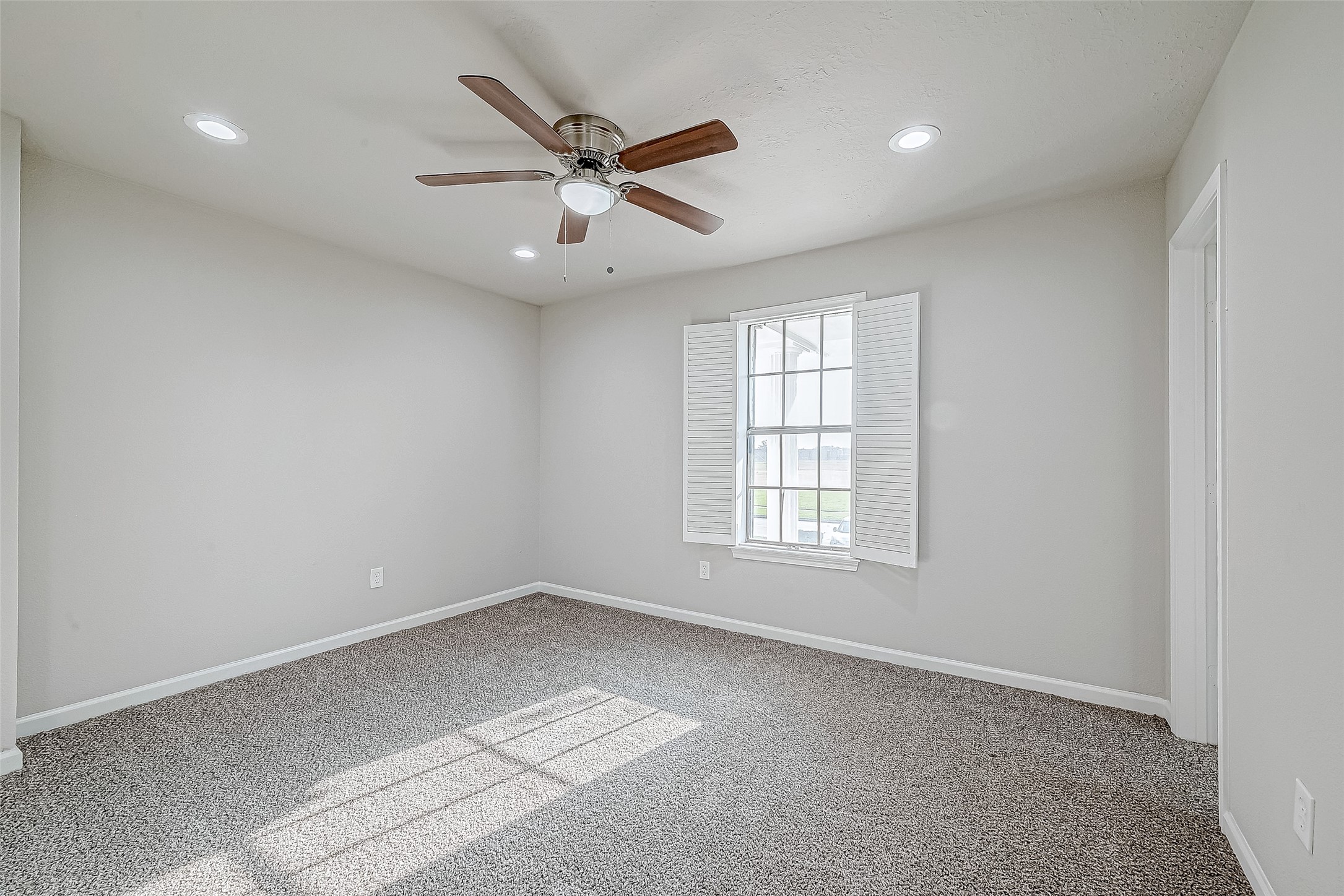 Airy bedroom with crisp white walls, a ceiling fan, and a window with shutters.