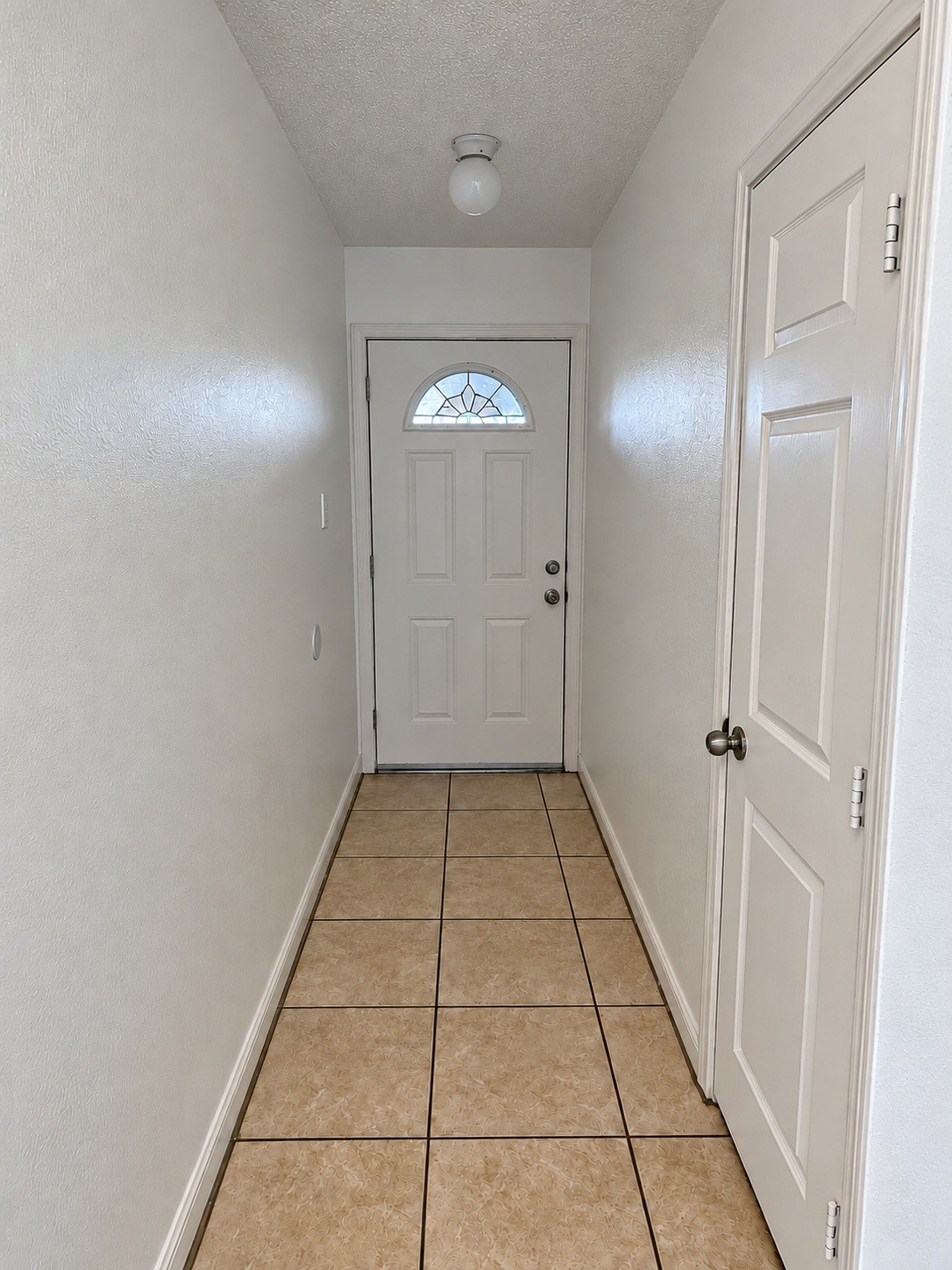 Interior entryway featuring neutral walls, tile flooring, and a front door with decorative glass detailing.