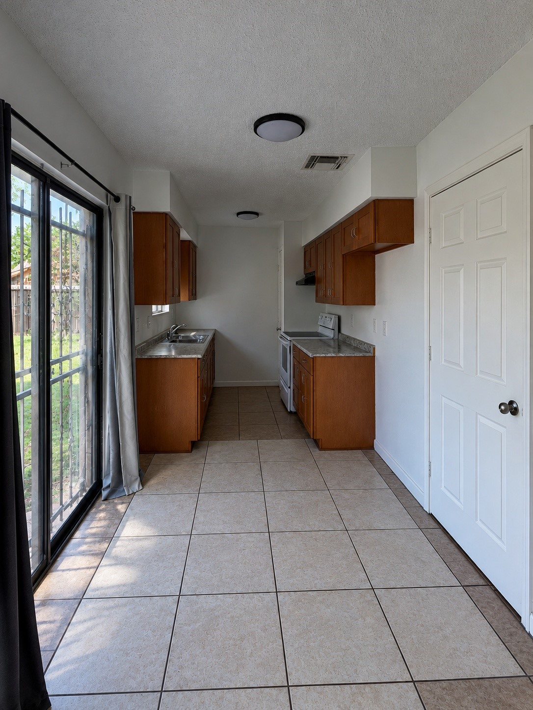 View of the kitchen and adjoining dining area featuring ceramic tile flooring, wood cabinetry, and a sliding glass door that provides natural light and access to the backyard. The dining area offers space for a table and chairs.