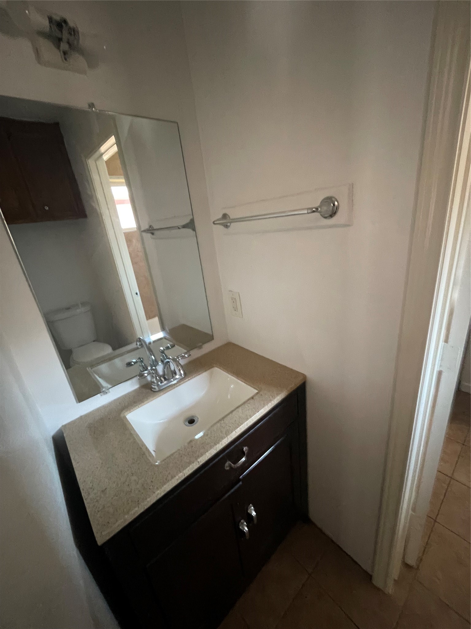 Half bathroom featuring a modern vanity with dark cabinetry, a white countertop, a large mirror, and neutral wall colors. A functional space that connects to the full bathroom.