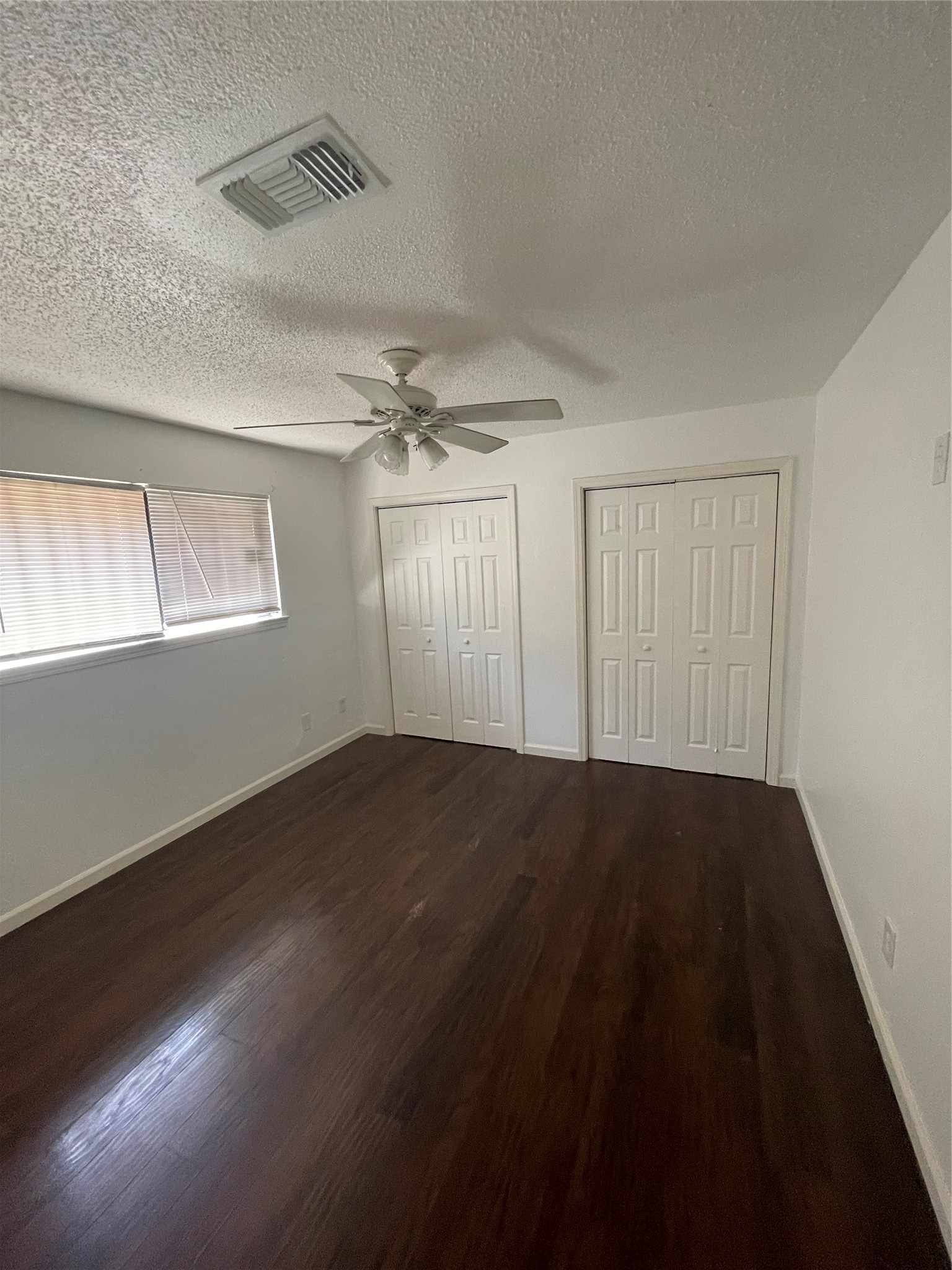 Spacious primary bedroom featuring wood look flooring, neutral wall colors, a ceiling fan, two closets offering additional storage, and windows that provide natural light. A comfortable and versatile space ready for your personal touch.