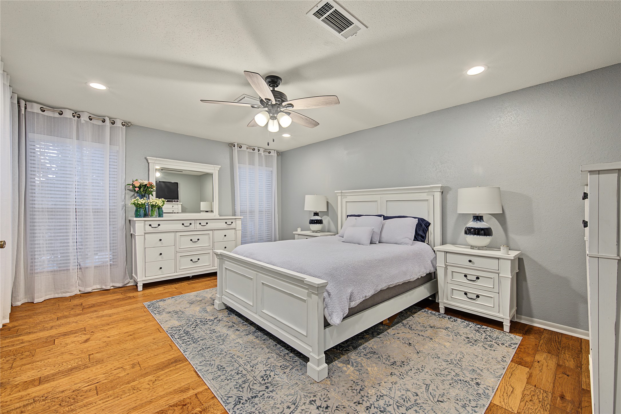 Spacious primary bedroom with wood look laminate flooring and ceiling fan Spacious primary bedroom with wood look laminate flooring and ceiling fan