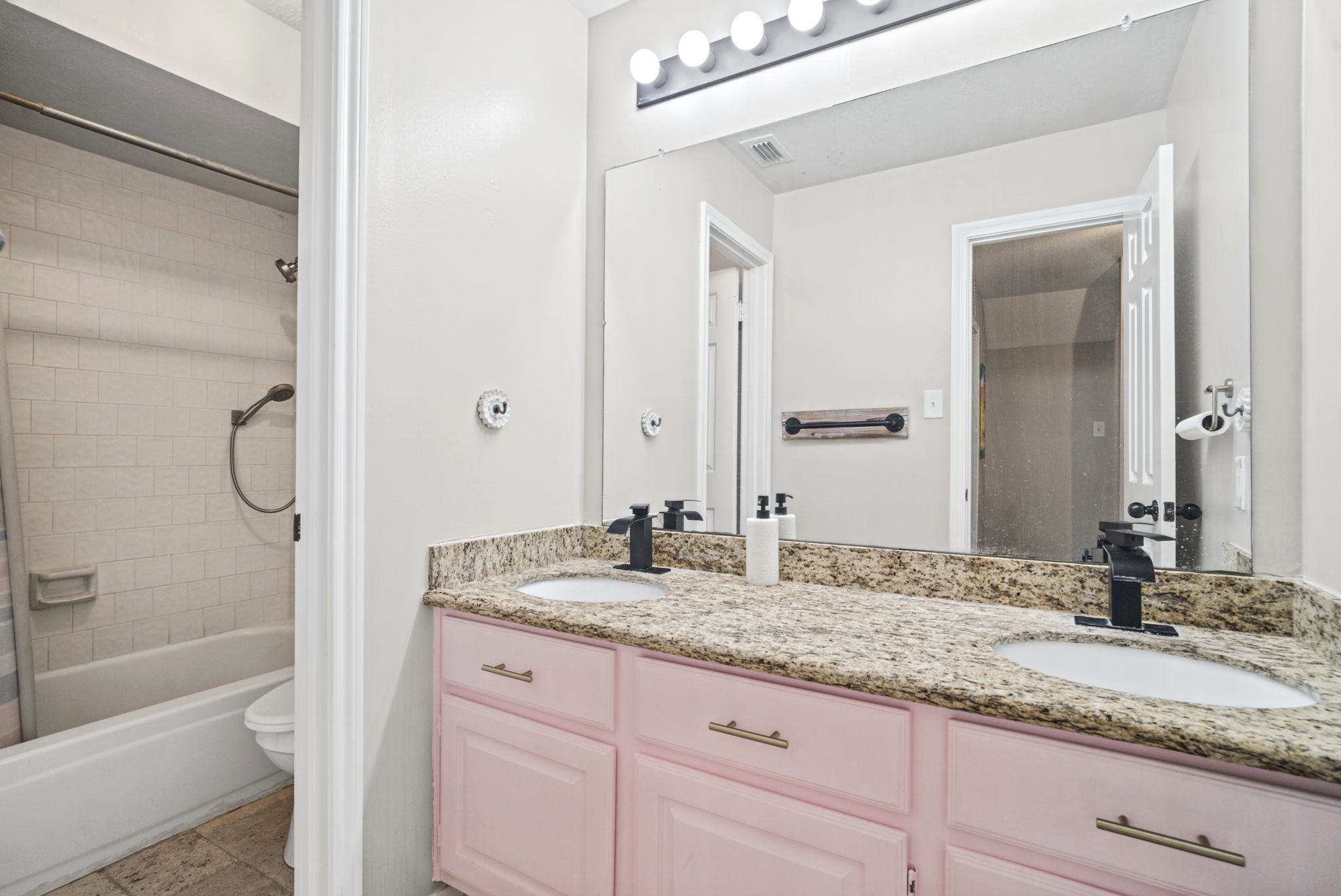 The upstairs secondary bathroom features a convenient separate vanity area, offering easy access to the sink without disturbing those using the shower or toilet. Charming light pink cabinetry paired with granite countertops adds a unique touch of character and style to this functional space.