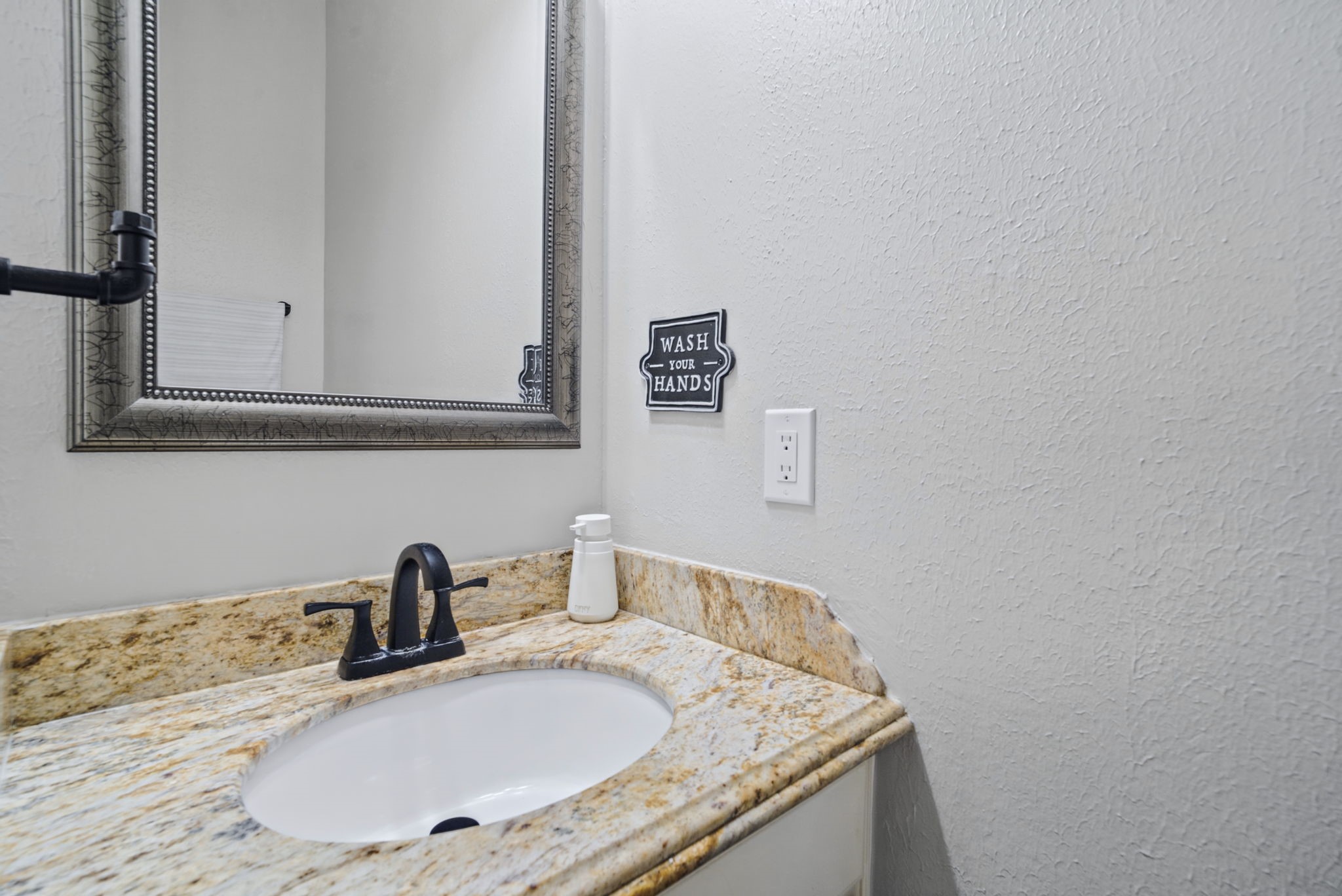 A convenient half bath is located just off the living room, featuring an elegant granite countertop and white cabinetry. Perfectly situated for guests, this stylish and functional space adds comfort and convenience when entertaining.