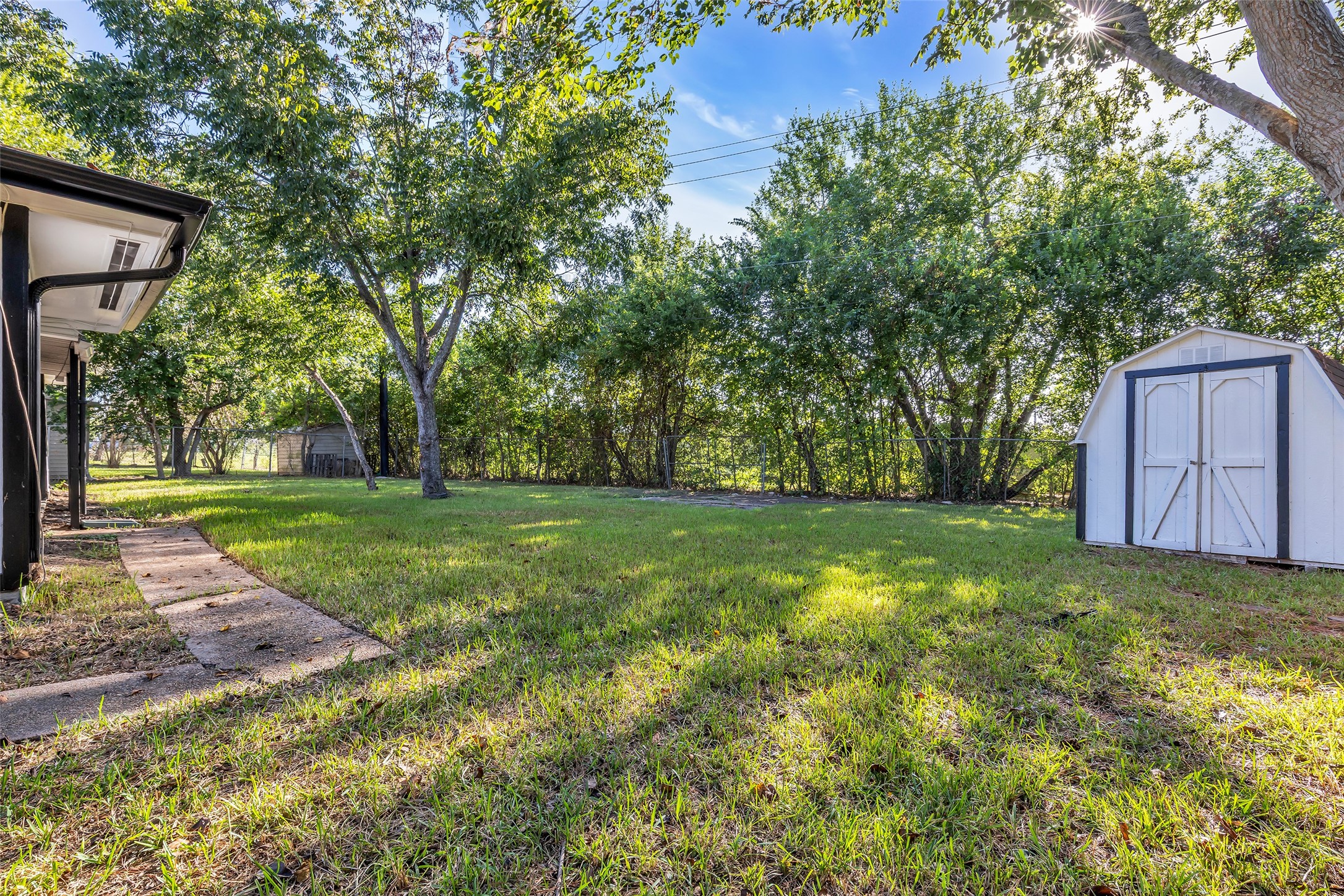 A spacious backyard with mature shade trees, a paver walkway and a storage shed for tools and gear.