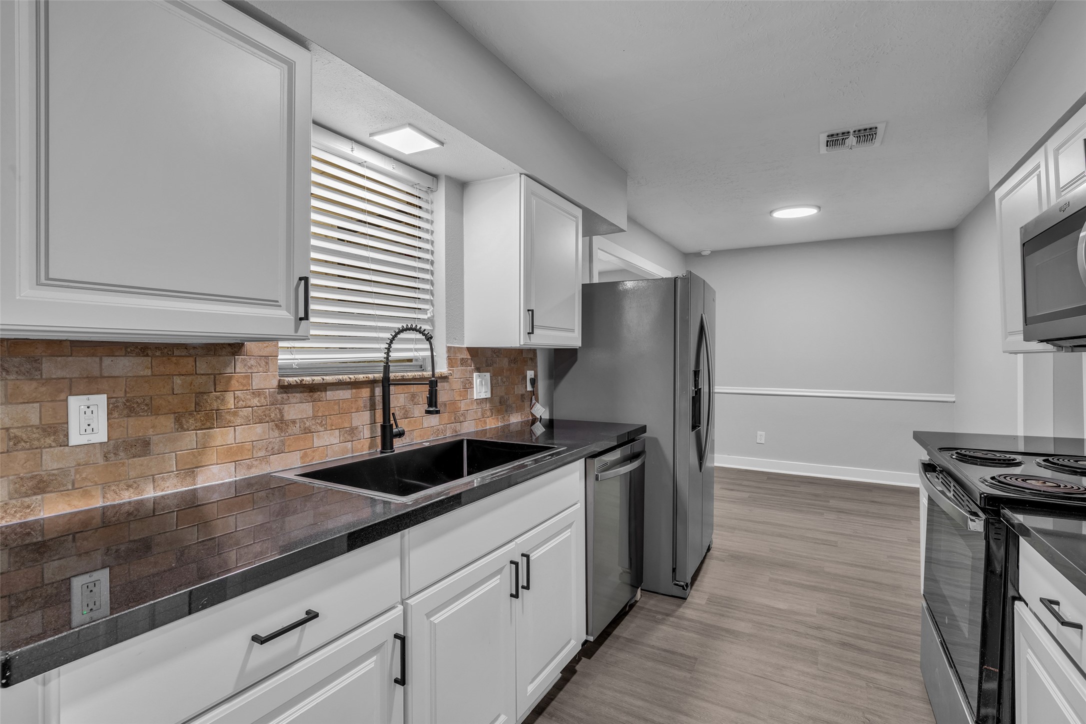 White cabinetry, dark countertops, stainless steel appliances and a stone-look tile backsplash make everyday cooking easy.