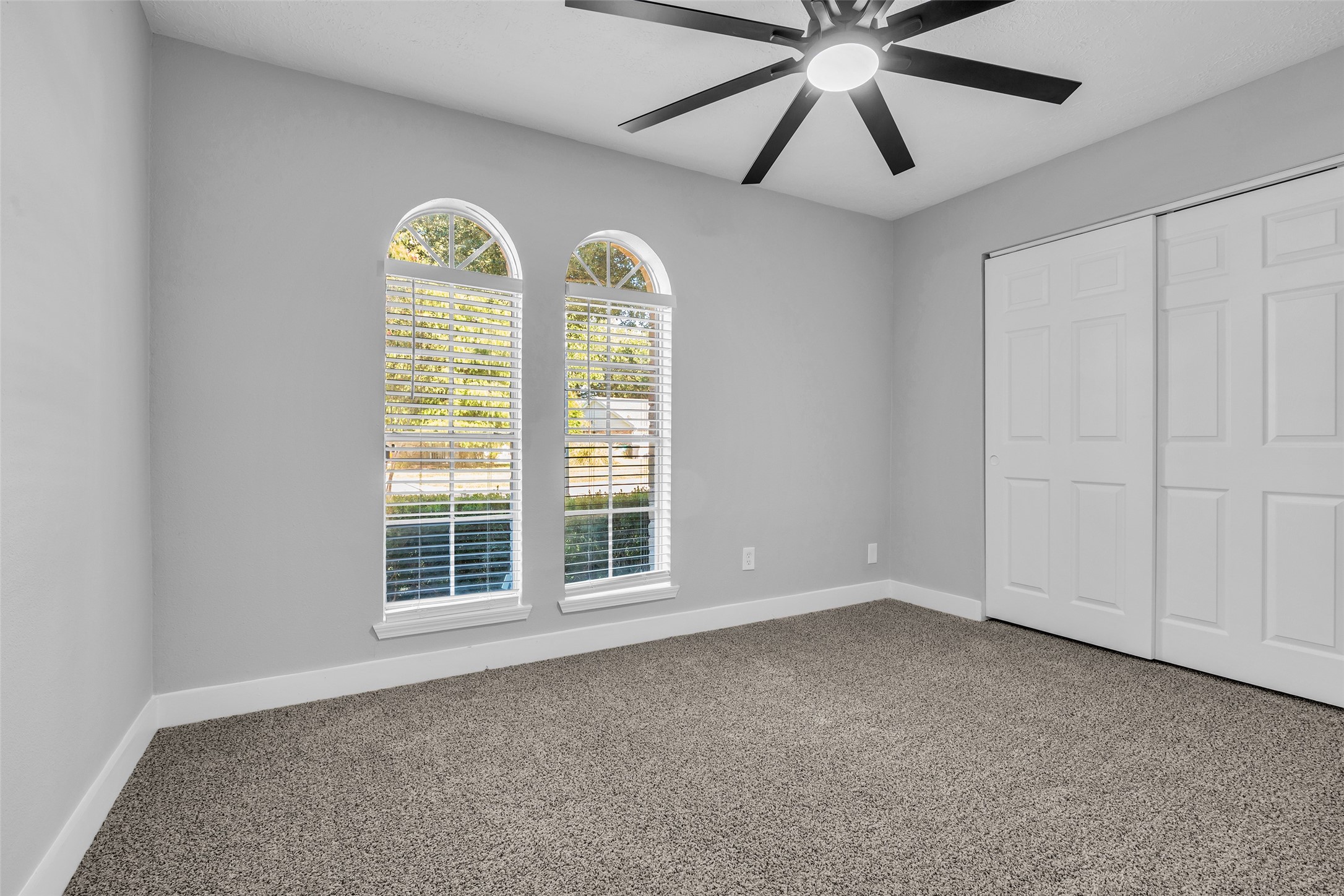 Twin arched windows fill this secondary bedroom with light, with a double-door closet for storage.
