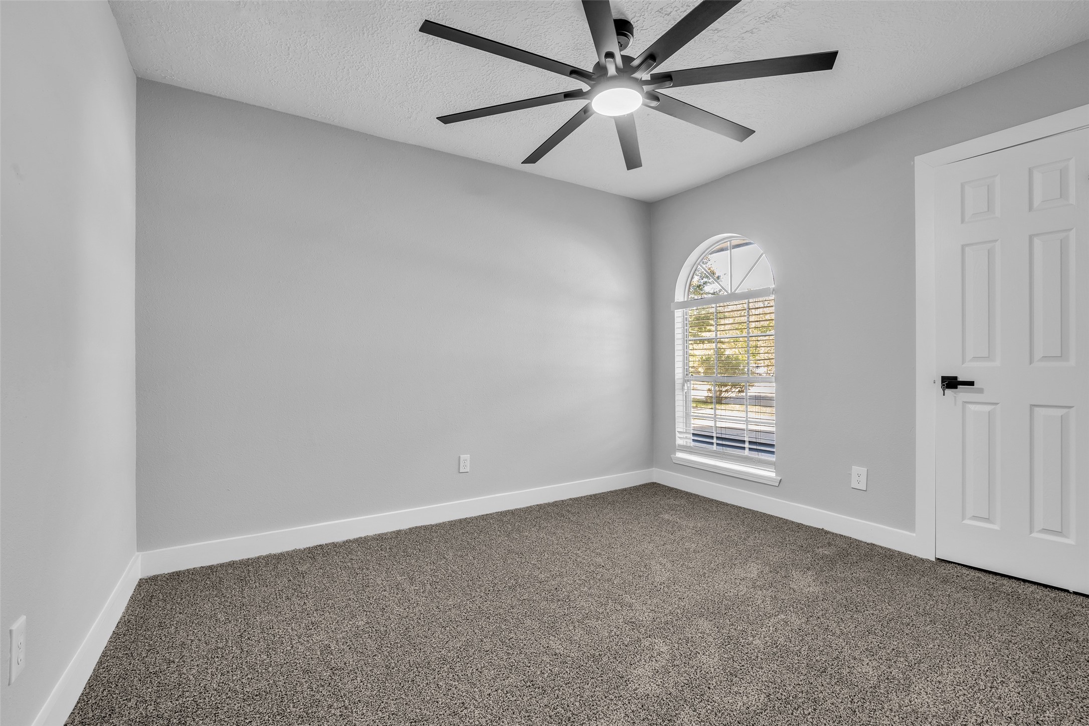 A cozy secondary bedroom with an arched window and a ceiling fan, ready for guests or a home office.