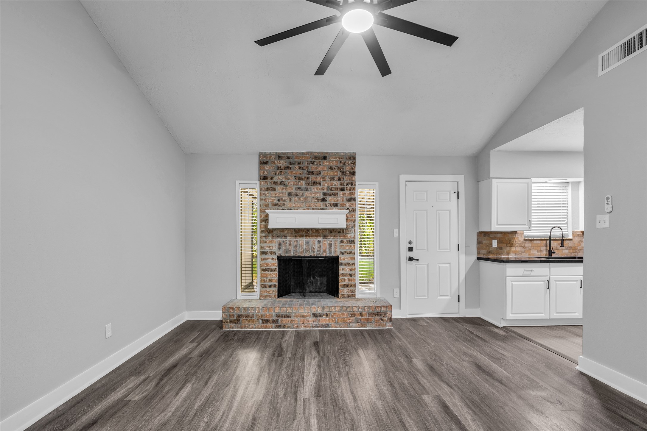 Gather around the brick fireplace with a white mantel, under a vaulted ceiling with a modern ceiling fan.