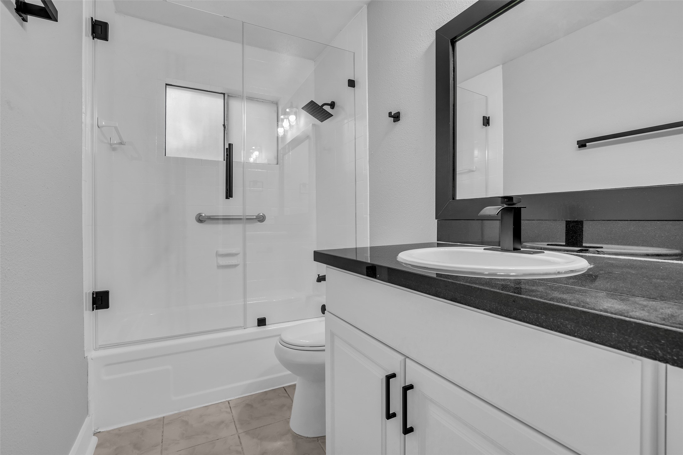 Start the day in the tub/shower with a glass enclosure, plus a white vanity with dark countertop and matte black hardware.