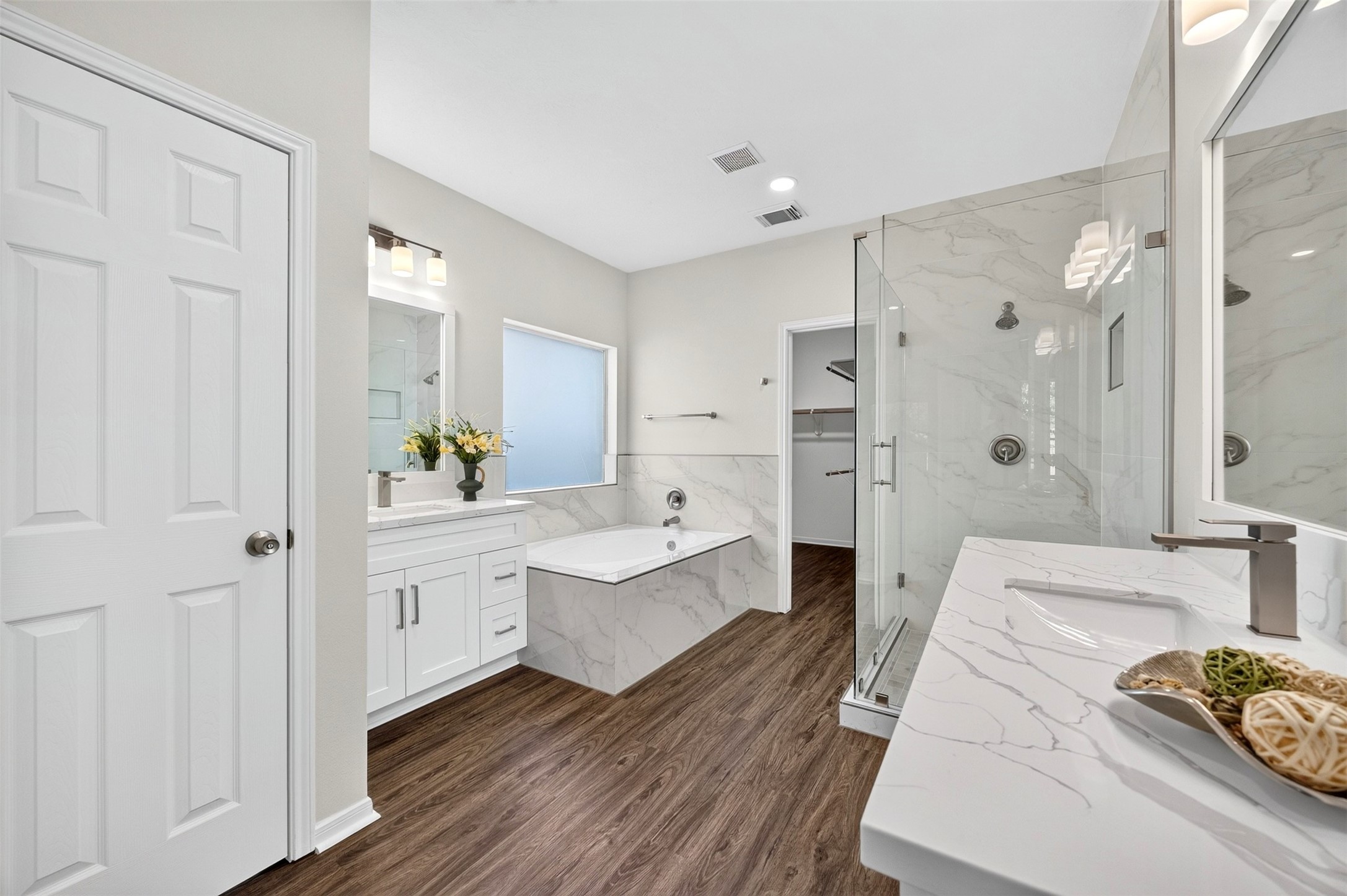 Elegant bathroom featuring a luxurious soaking tub, spacious glass-enclosed shower, and dual vanities with sleek marble countertops