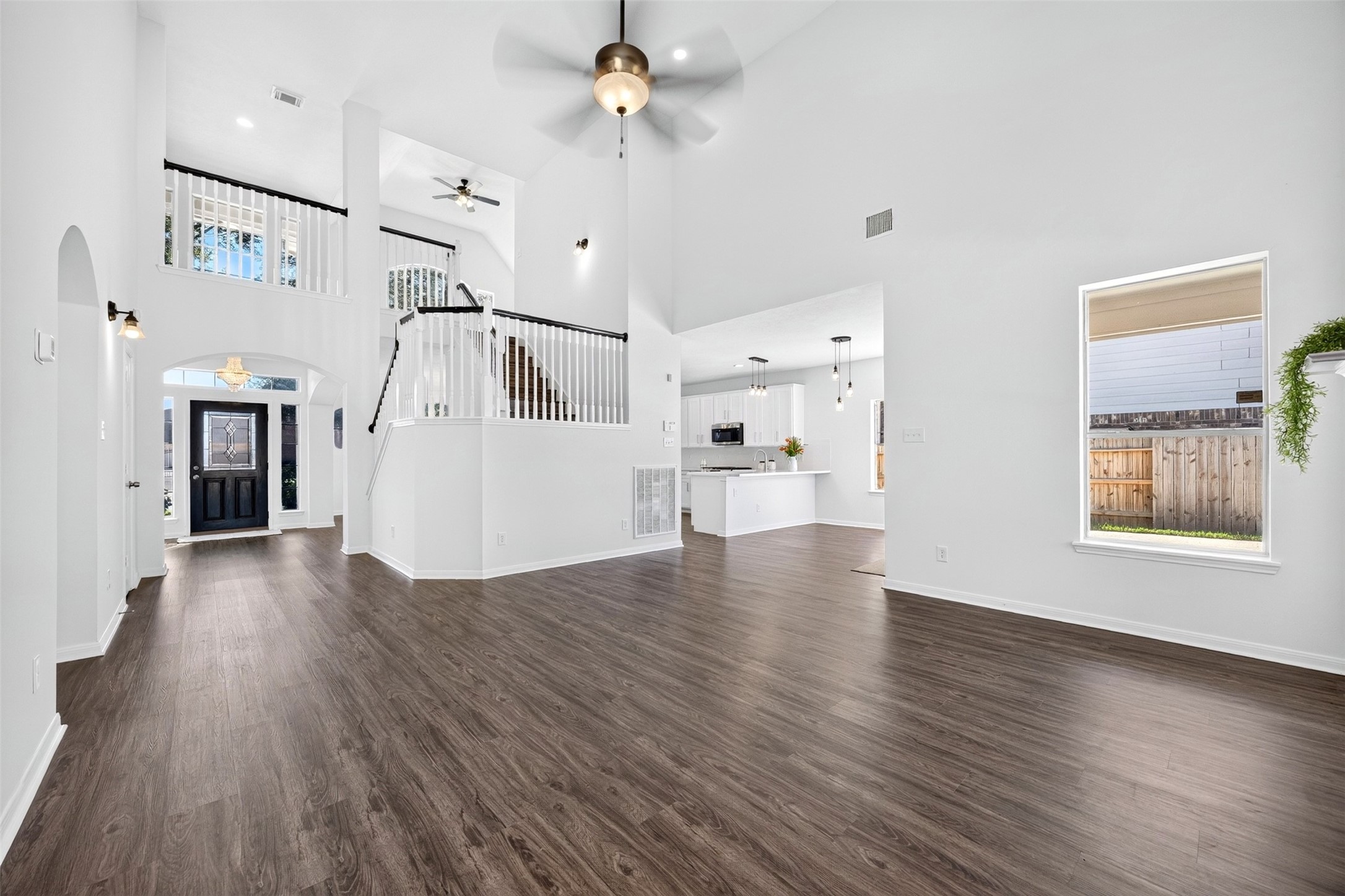 Spacious open-concept living area with high ceilings, elegant staircase, and abundant natural light, seamlessly leading to a modern kitchen and inviting entryway.