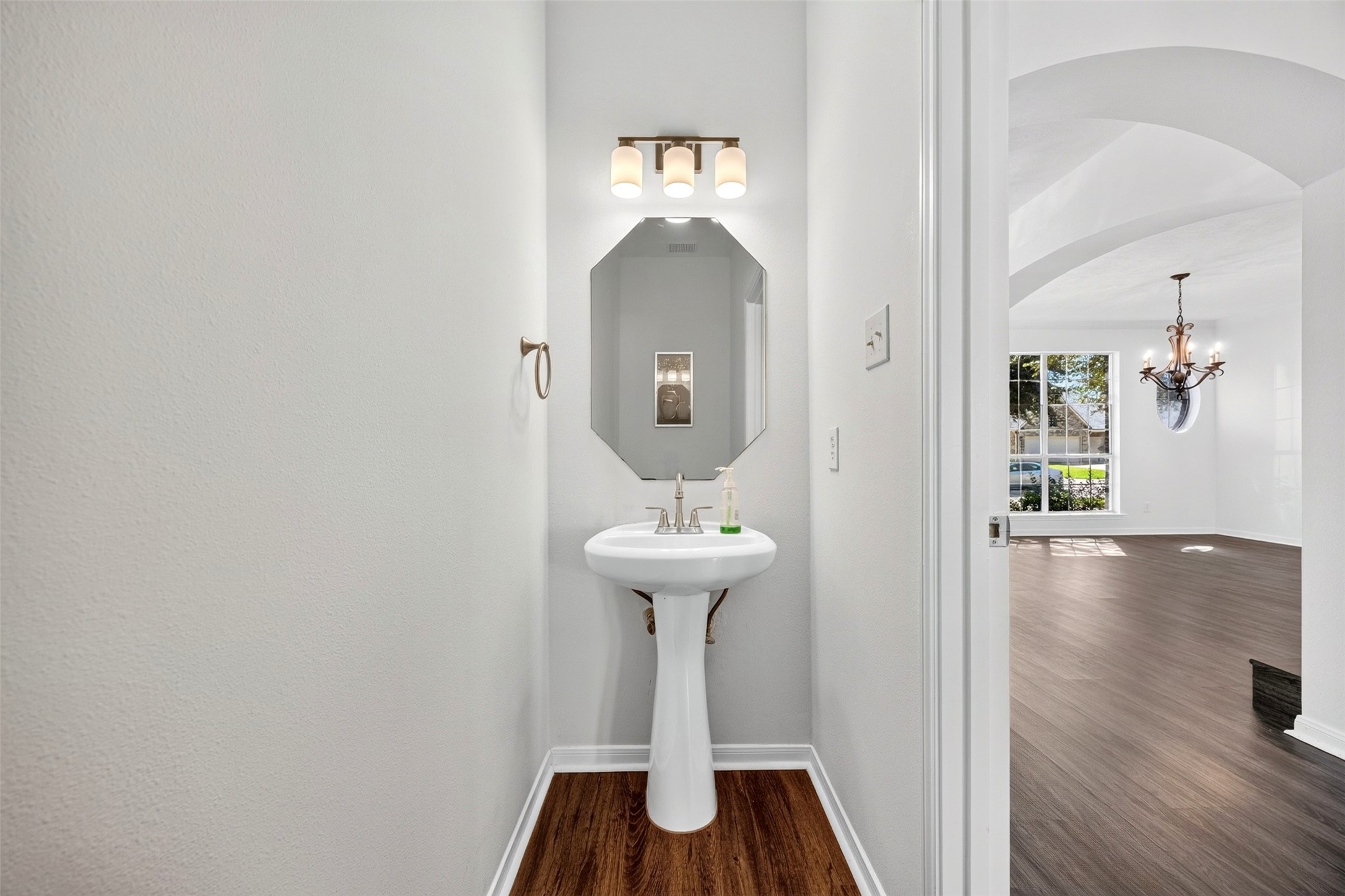 Charming powder room with a sleek pedestal sink, elegant lighting, and a modern octagonal mirror