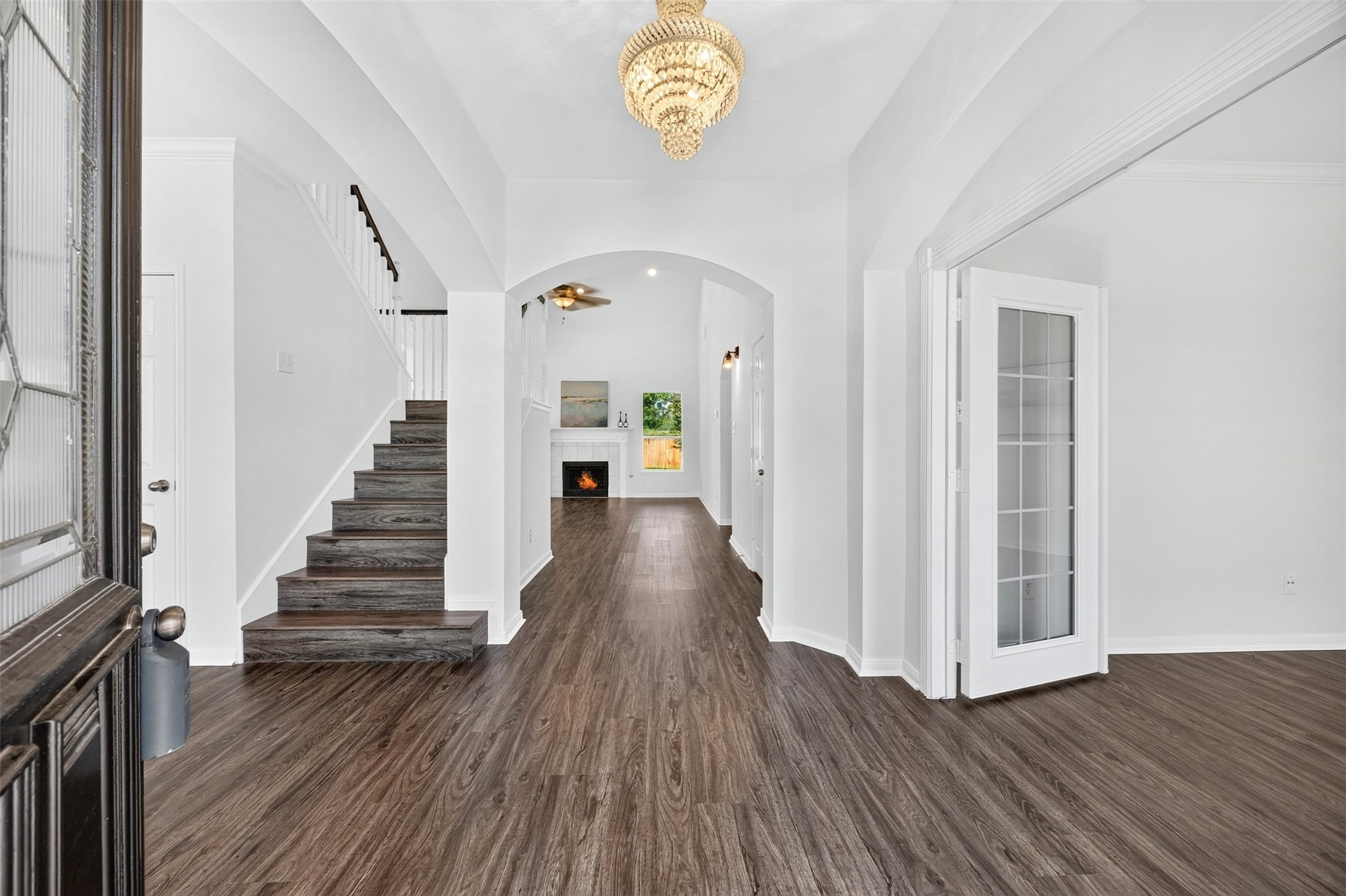 Elegant entryway featuring luxury vinyl plank flooring, a stunning chandelier, and a welcoming staircase leading to the upper level. The open floor plan seamlessly connects to a cozy living area with a fireplace, creating an inviting atmosphere.