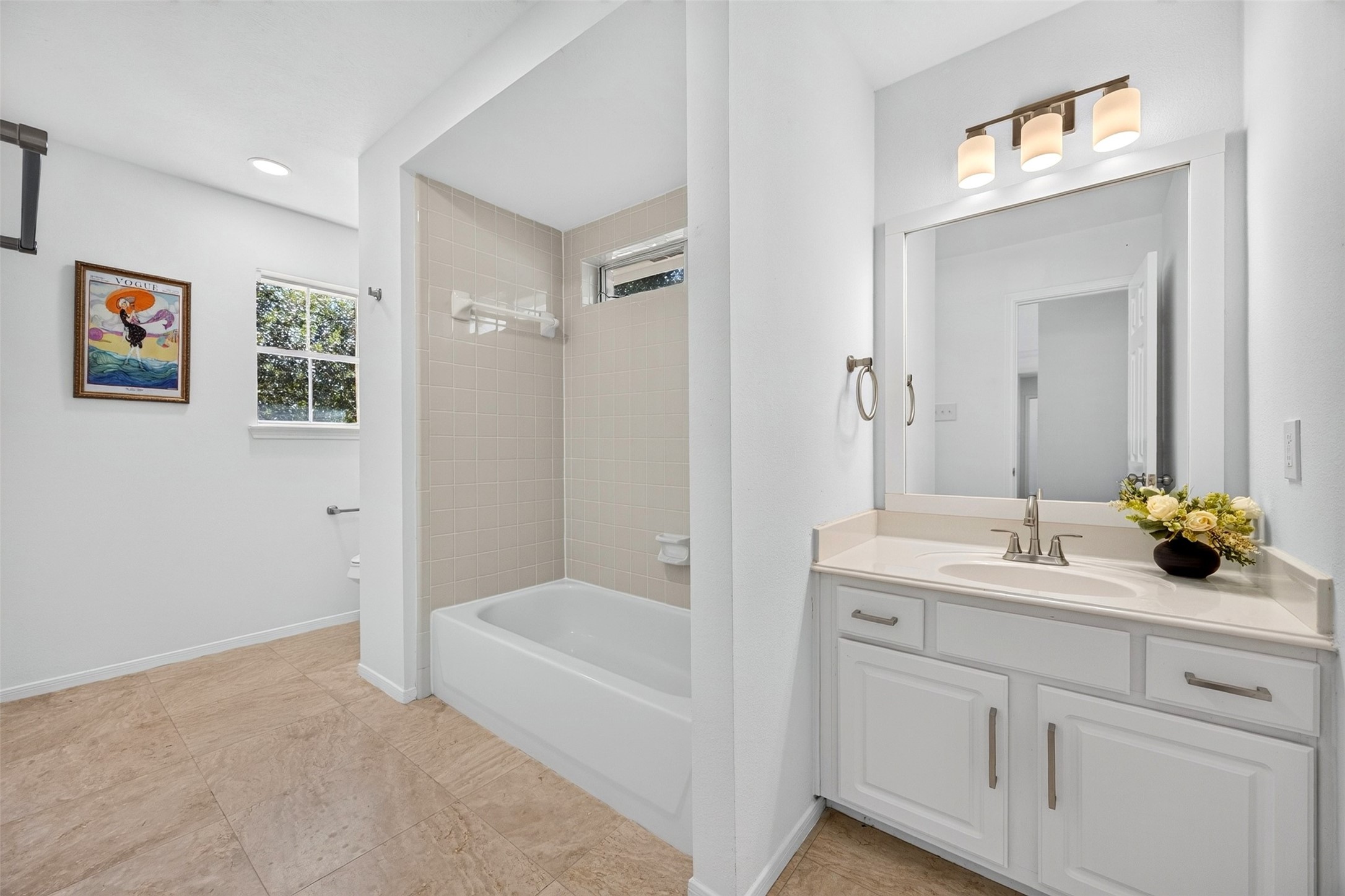 Bright and inviting bathroom featuring a modern vanity with ample storage, a classic bathtub, and elegant tile flooring, enhanced by natural light from the window.