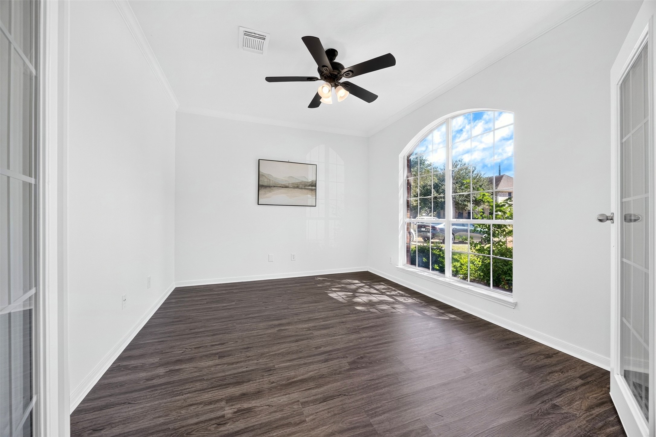 Spacious office room with elegant French doors and a ceiling fan, offering a versatile space filled with natural light