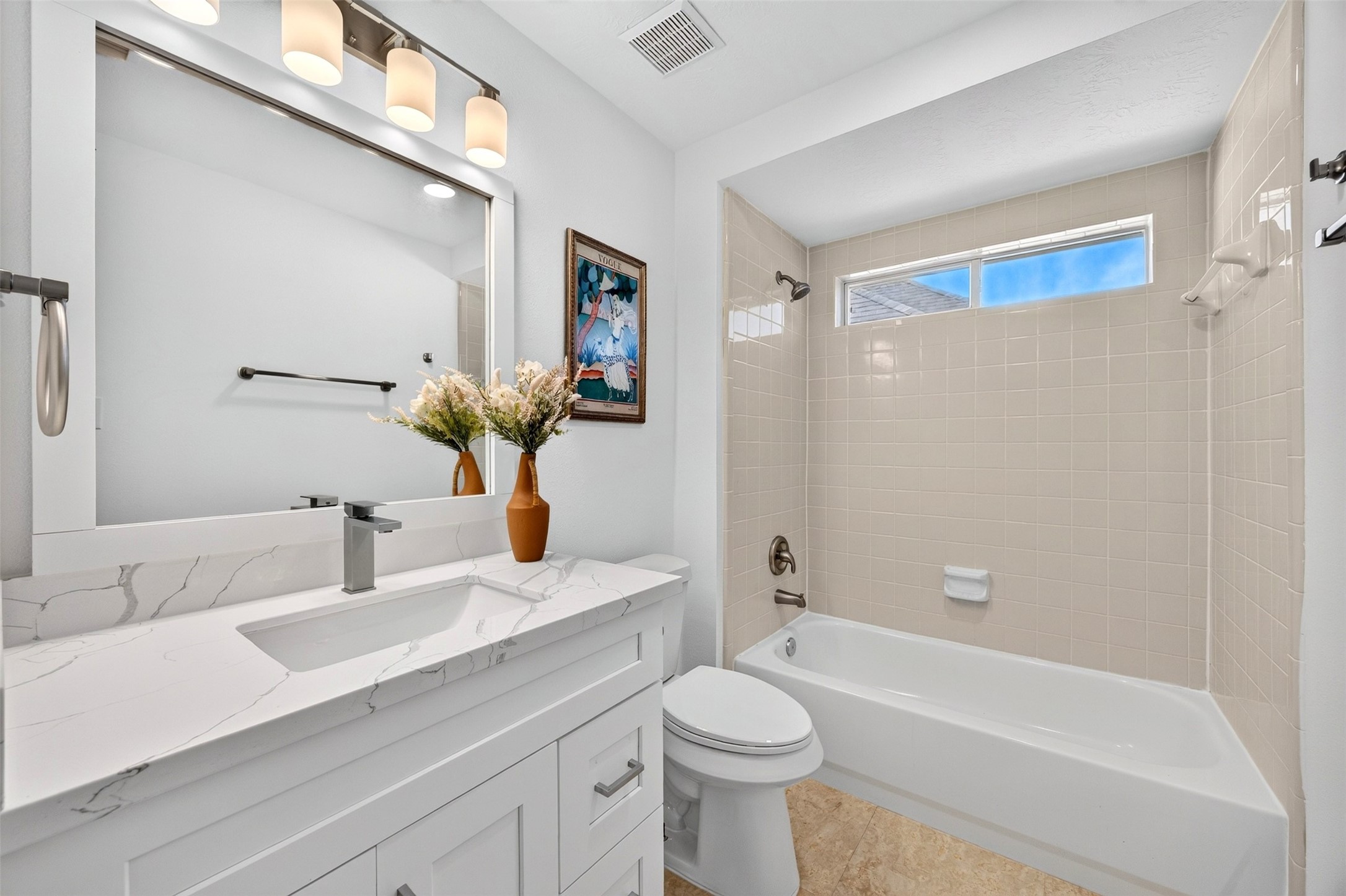 Bright and modern bathroom featuring a sleek vanity with a marble countertop, elegant lighting, and a cozy bathtub beneath a high window for natural light.