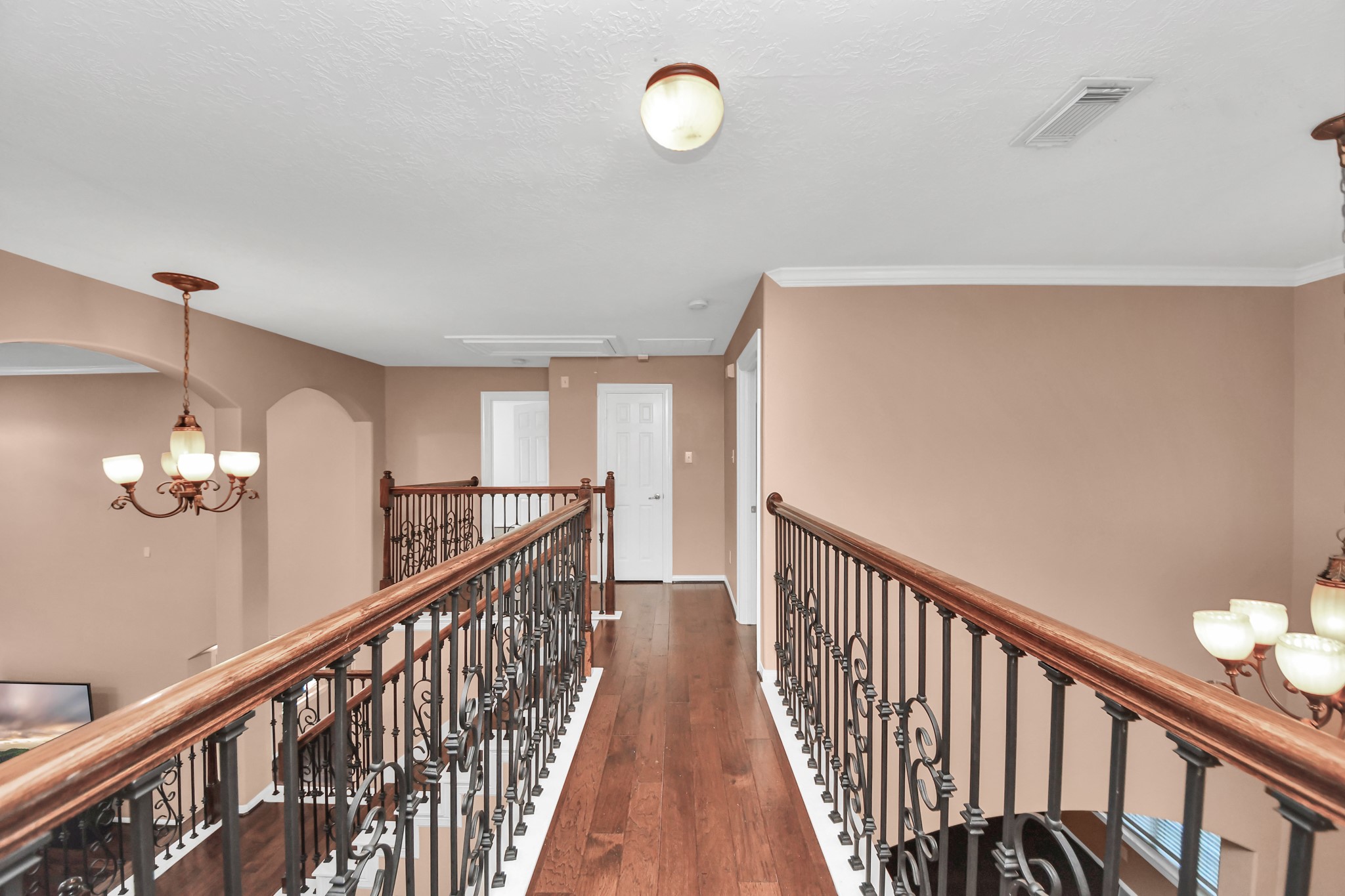 Elegant upstairs hallway featuring rich hardwood floors and stylish wrought-iron railings, complemented by soft, ambient lighting.