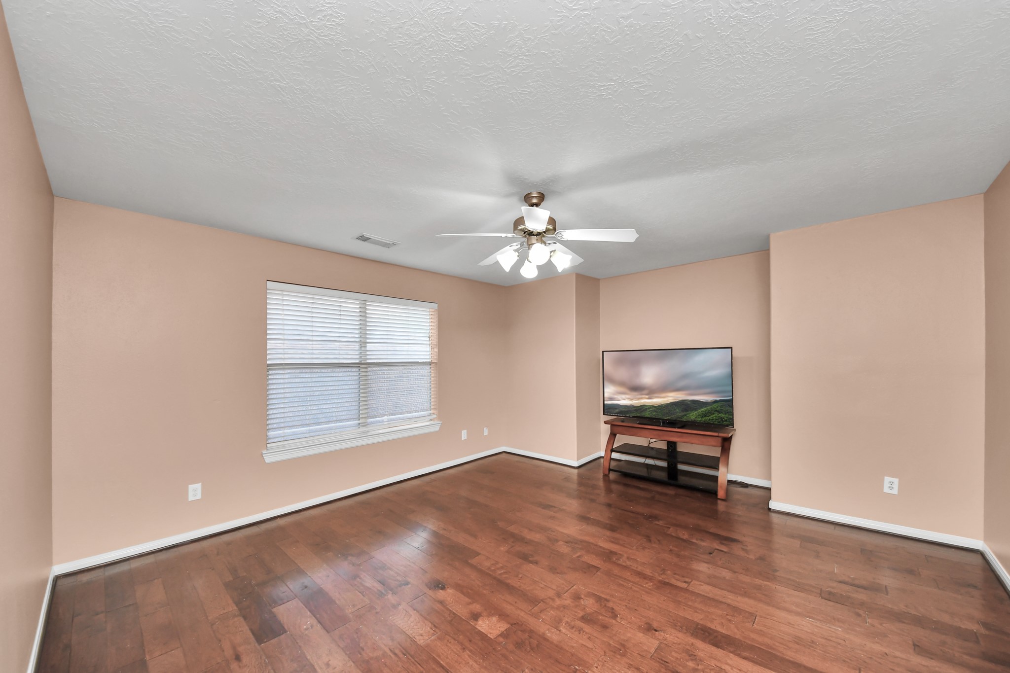 Spacious MEDIA /GAME ROOM area with warm hardwood floors, abundant natural light from a large window, and a ceiling fan for comfort.