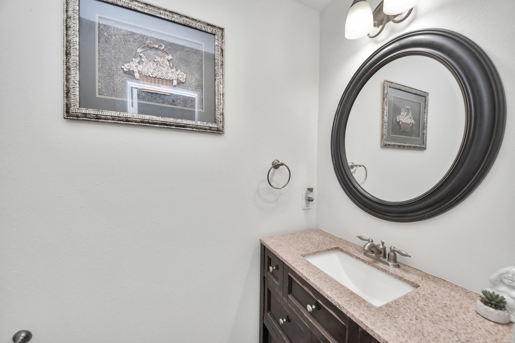 Charming powder room with a sleek granite countertop, elegant dark wood vanity, and a stylish round mirror, complemented by tasteful wall art and modern lighting.