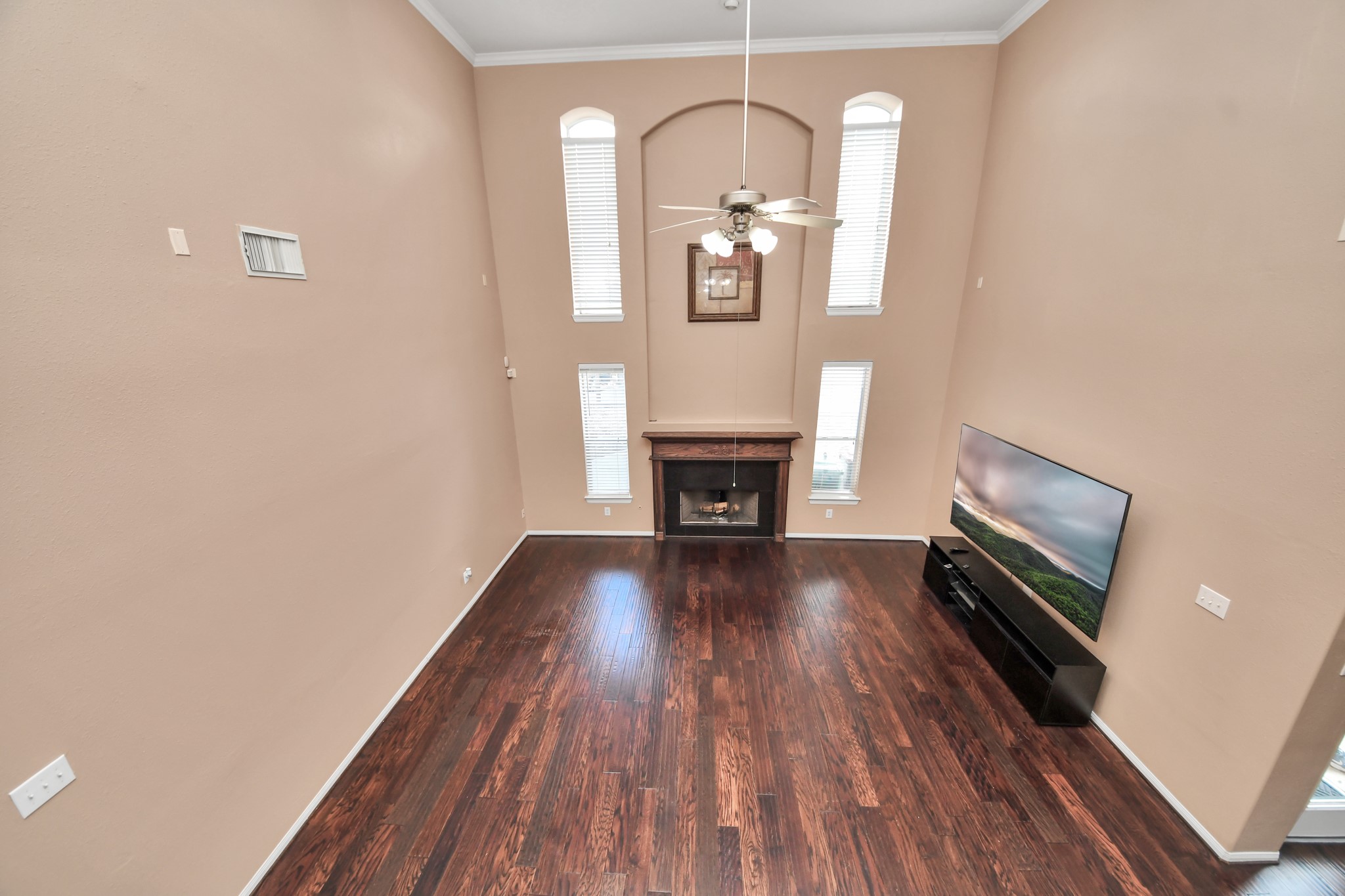 Spacious living room with soaring ceilings, rich hardwood floors, and abundant natural light from tall windows, featuring a cozy fireplace and modern ceiling fan.