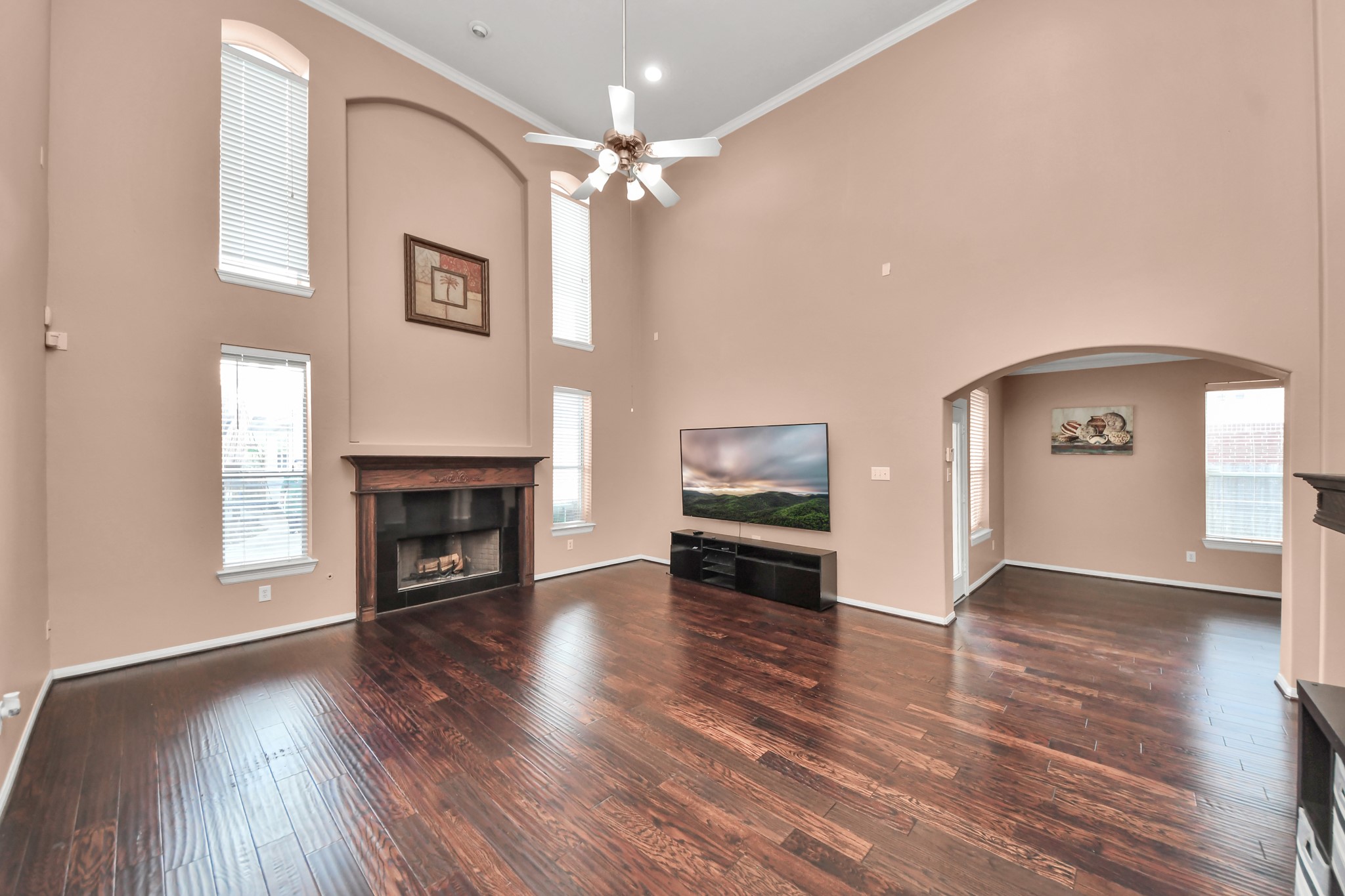 Spacious living room with soaring ceilings, rich hardwood floors, and abundant natural light, featuring a cozy fireplace and elegant arched entryway. Spacious living room with soaring ceilings, rich hardwood floors, and abundant natural light, featuring a cozy fireplace and elegant arched entryway.
