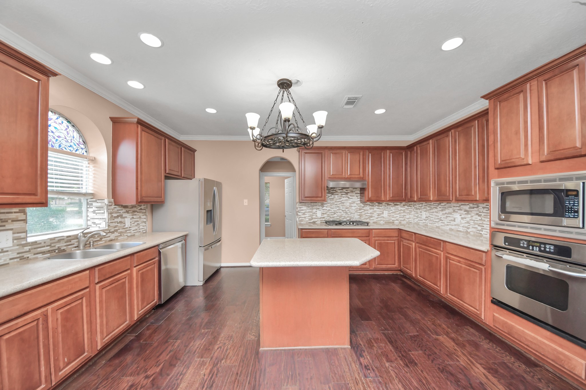 Spacious kitchen featuring rich wood cabinetry, sleek stainless steel appliances, and elegant tile backsplash, complete with a central island and stylish chandelier. Spacious kitchen featuring rich wood cabinetry, sleek stainless steel appliances, and elegant tile backsplash, complete with a central island and stylish chandelier.