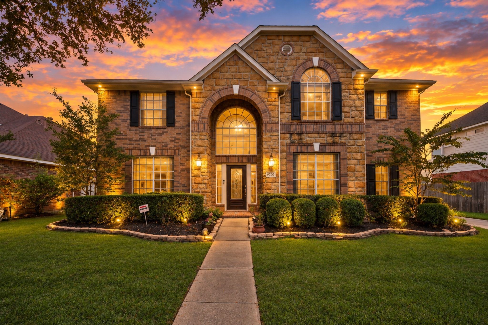VIRTUAL STAGING
Elegant two-story brick home with a grand arched entrance, beautifully landscaped front yard, and inviting evening ambiance.