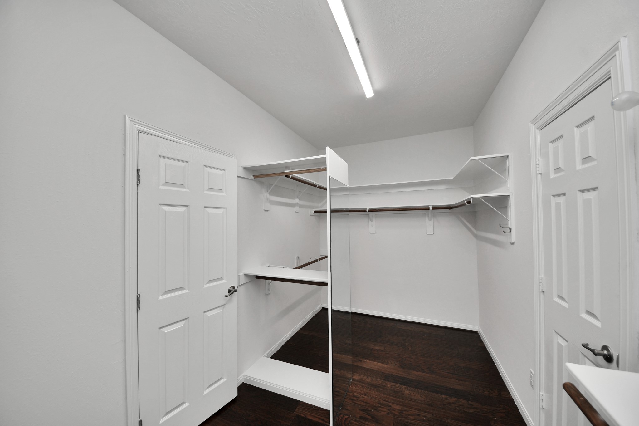 Spacious walk-in closet with dark hardwood floors, ample shelving, and hanging space, perfect for organizing your wardrobe.