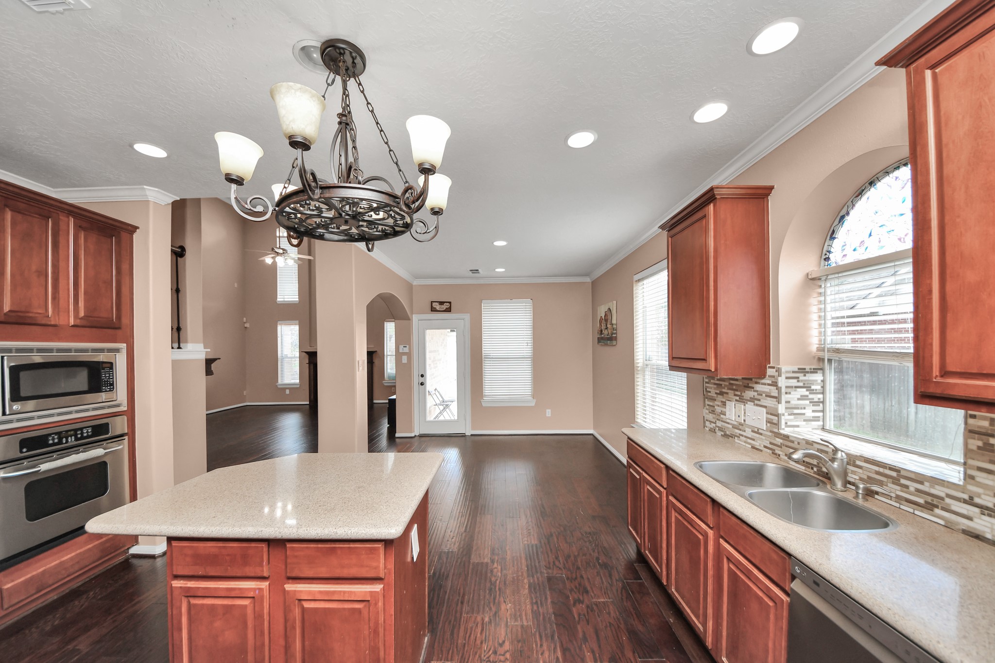 Spacious kitchen featuring warm wood cabinetry, a central island with elegant countertops, and a stylish chandelier.