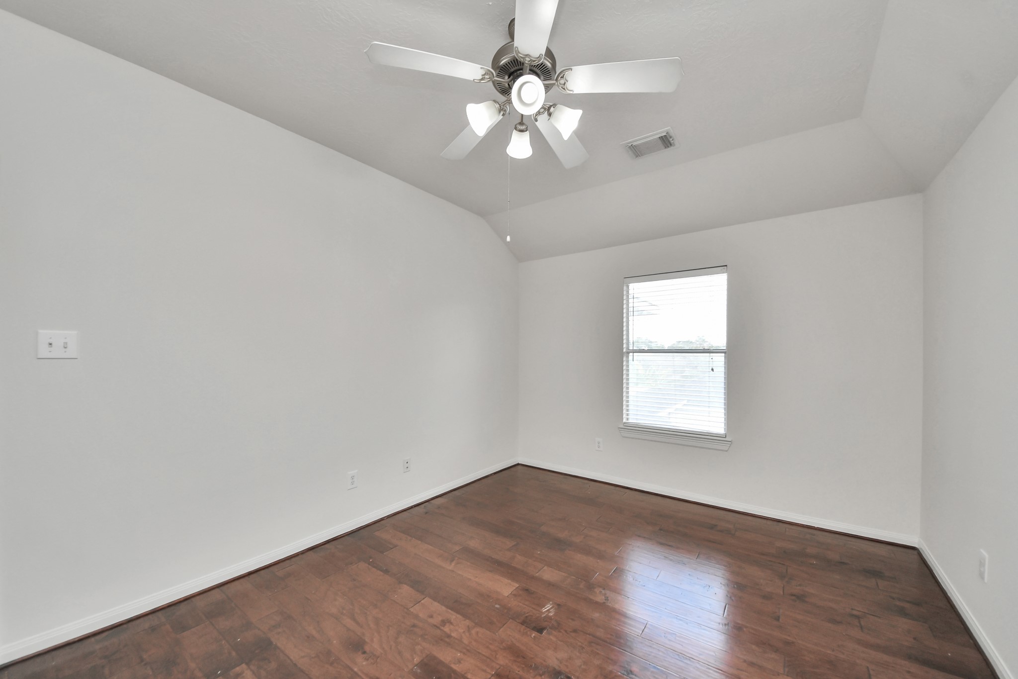 Bright room with rich hardwood floors, a ceiling fan, and a window offering natural light.