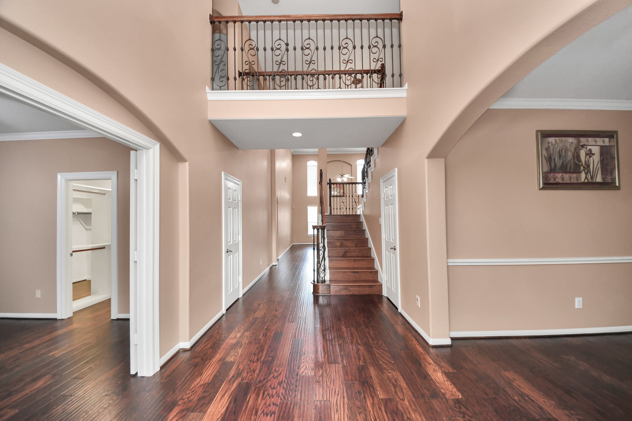 Elegant entryway with rich hardwood floors, a striking staircase, and a second-story overlook accented by ornate iron railings.