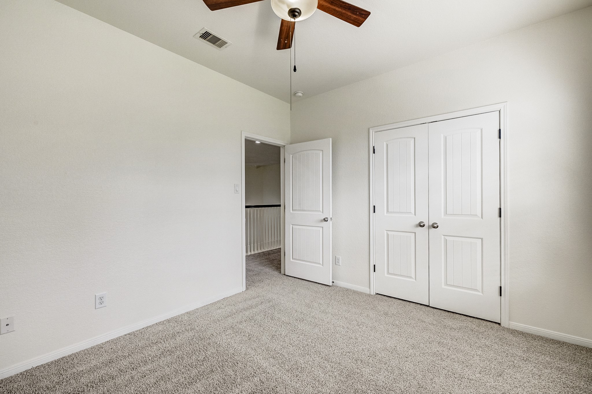 Bright, spacious bedroom featuring plush carpeting, a ceiling fan, and ample closet space with double doors.